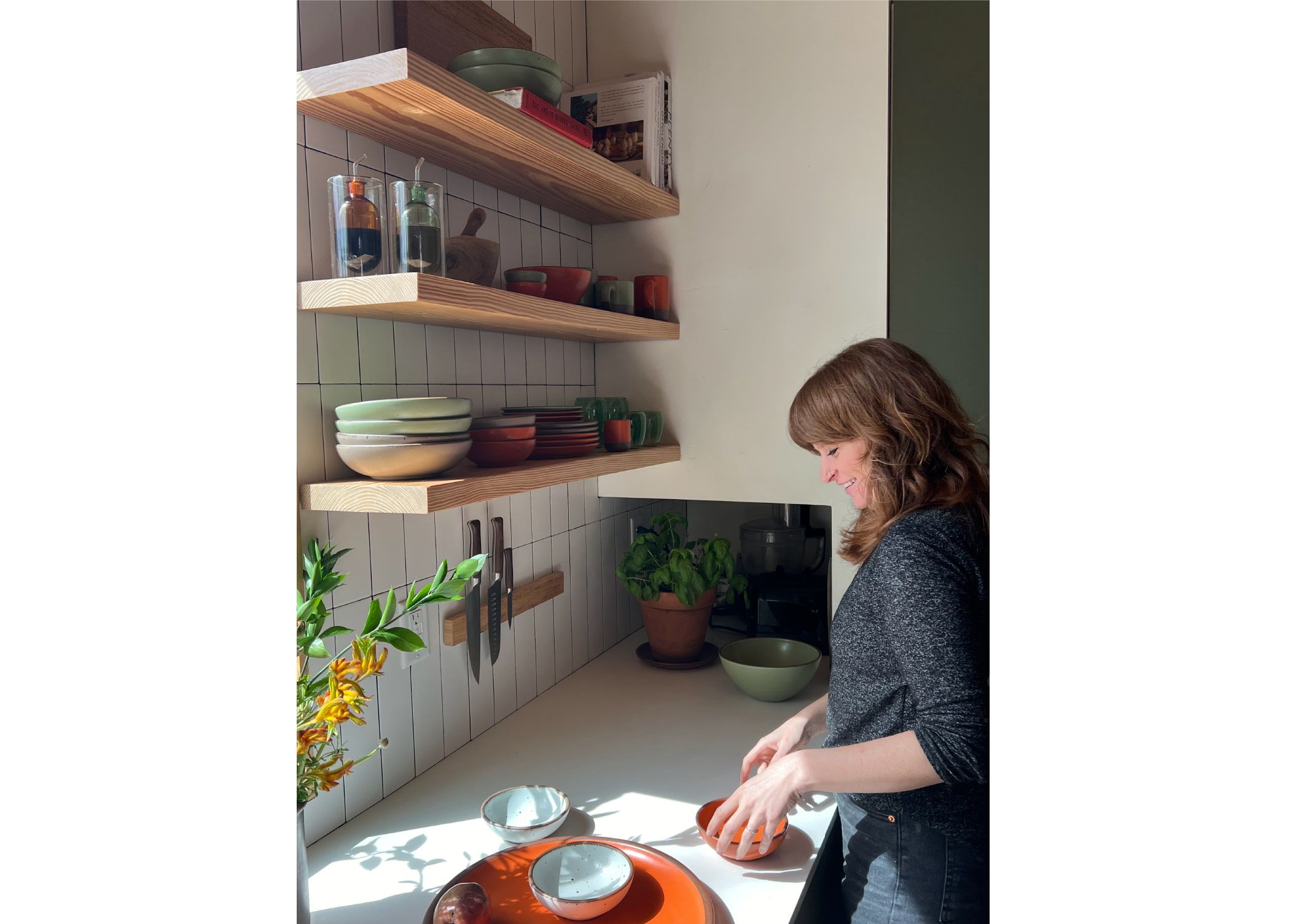 Nicole is arranging ceramic bowls in a bold orange color in a kitchen.