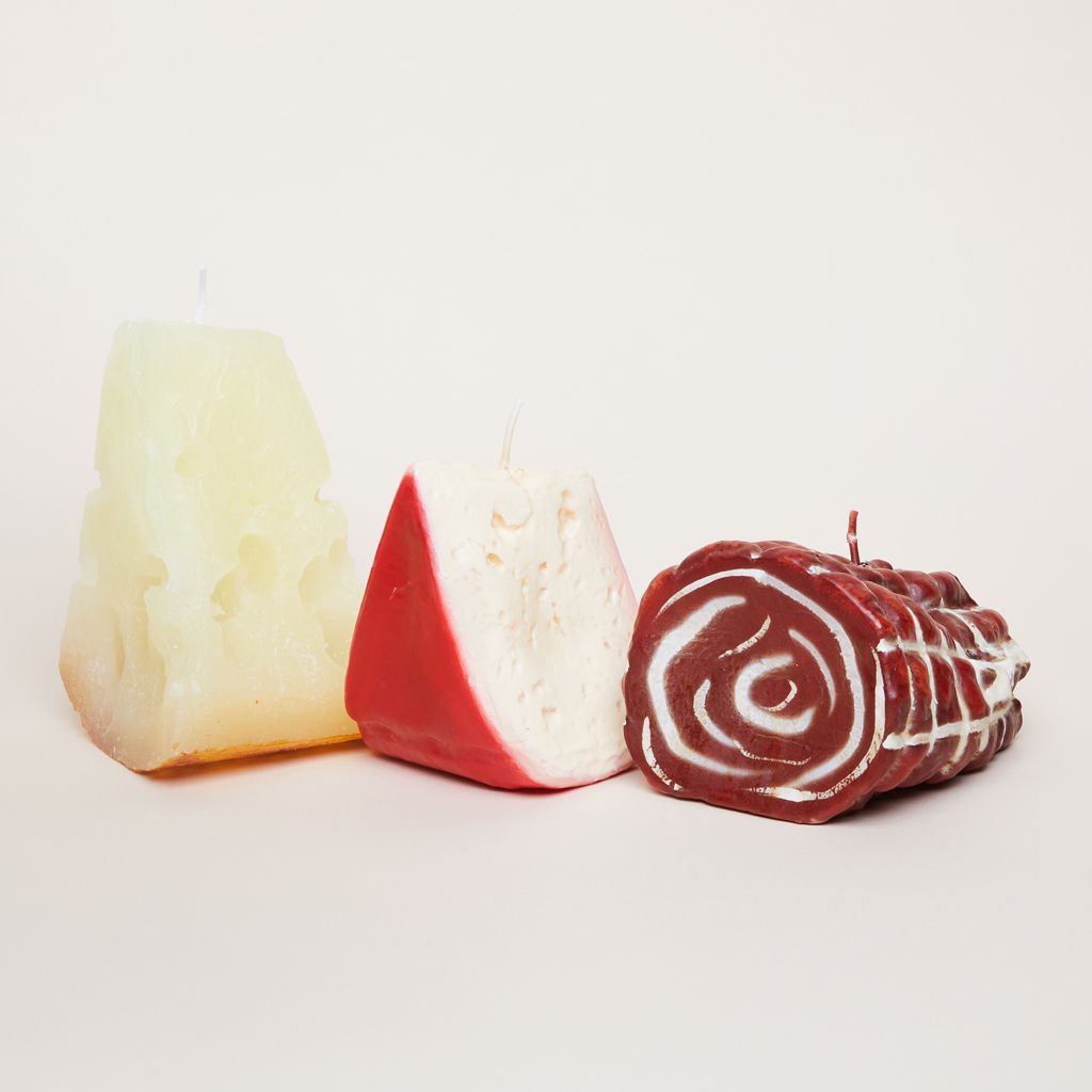 From left to right, a pale yellow candle that looks like gruyere, a pale yellow and red candle that looks like gouda and a red and white candle that looks like capicola