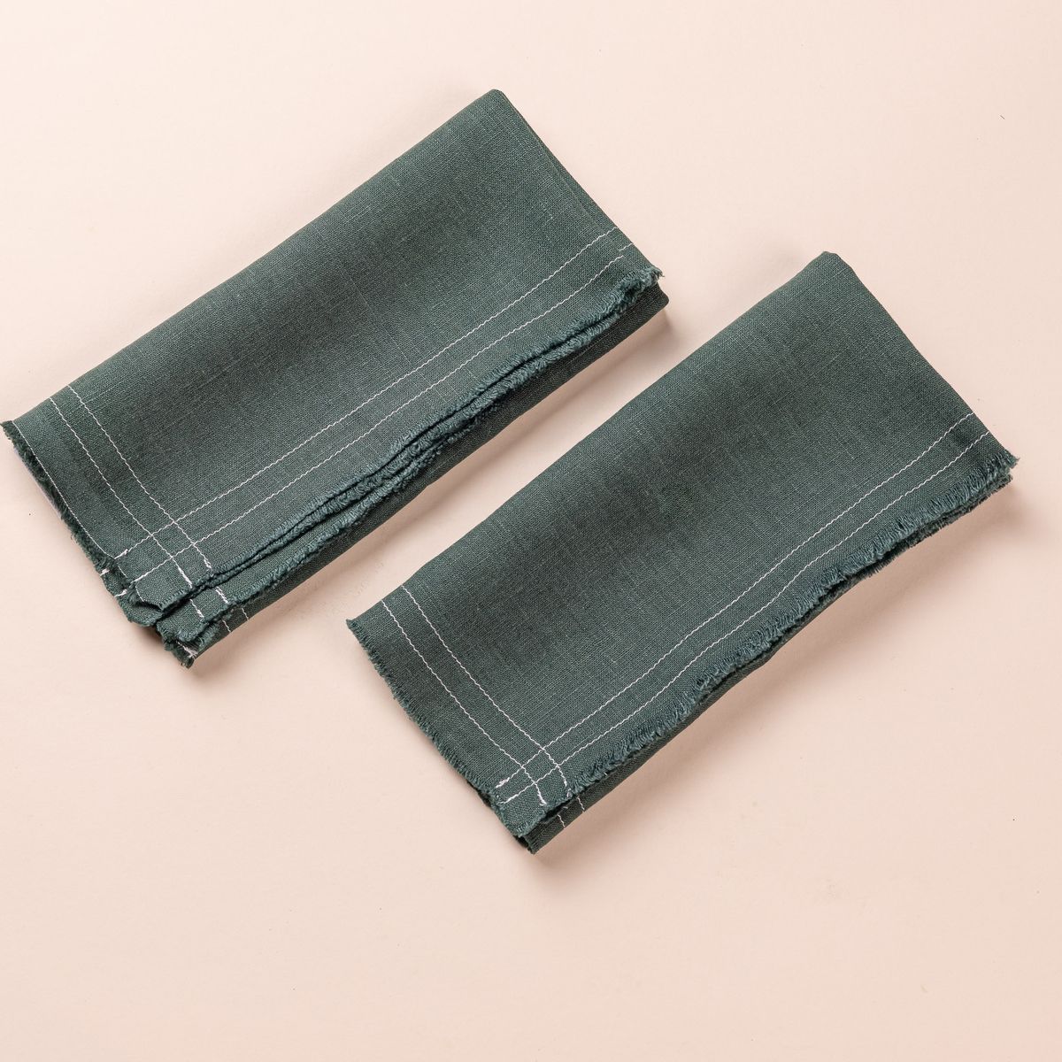 A folded deep teal pair of linen napkins with fringe edges