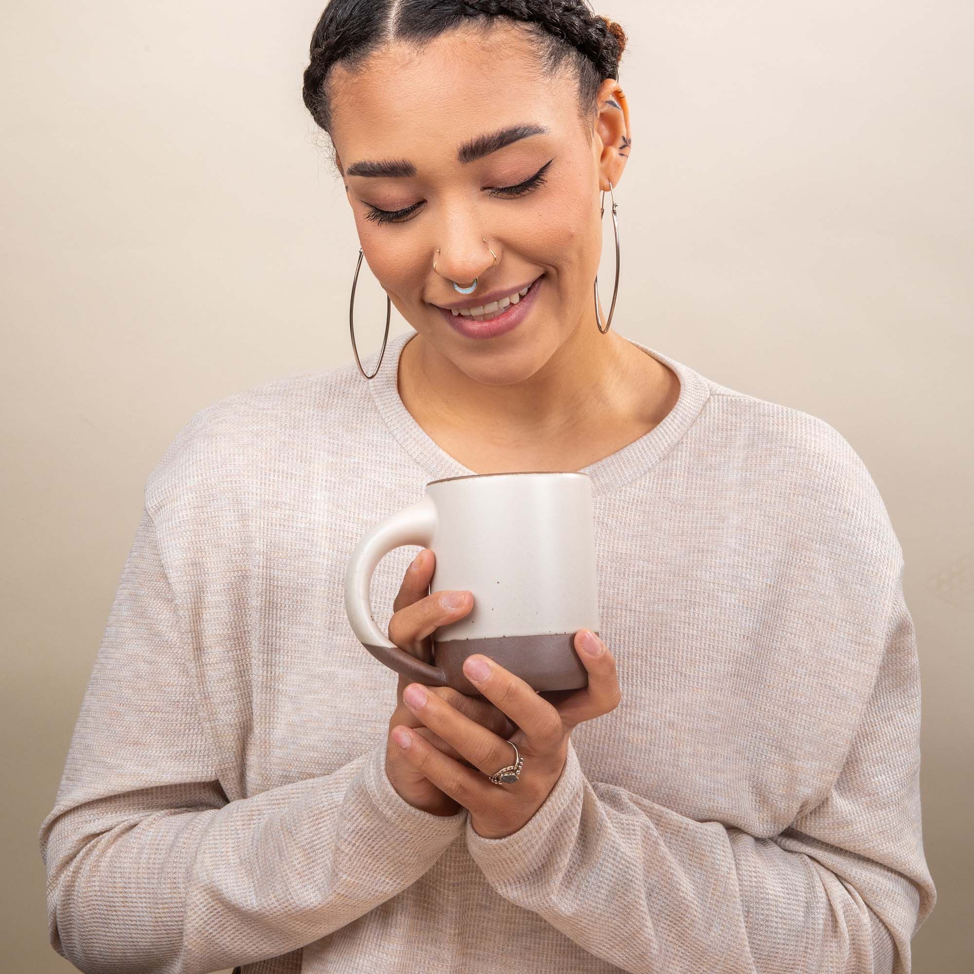 A woman holds an East Fork Mug in a cool white color and is looking at the mug smiling.