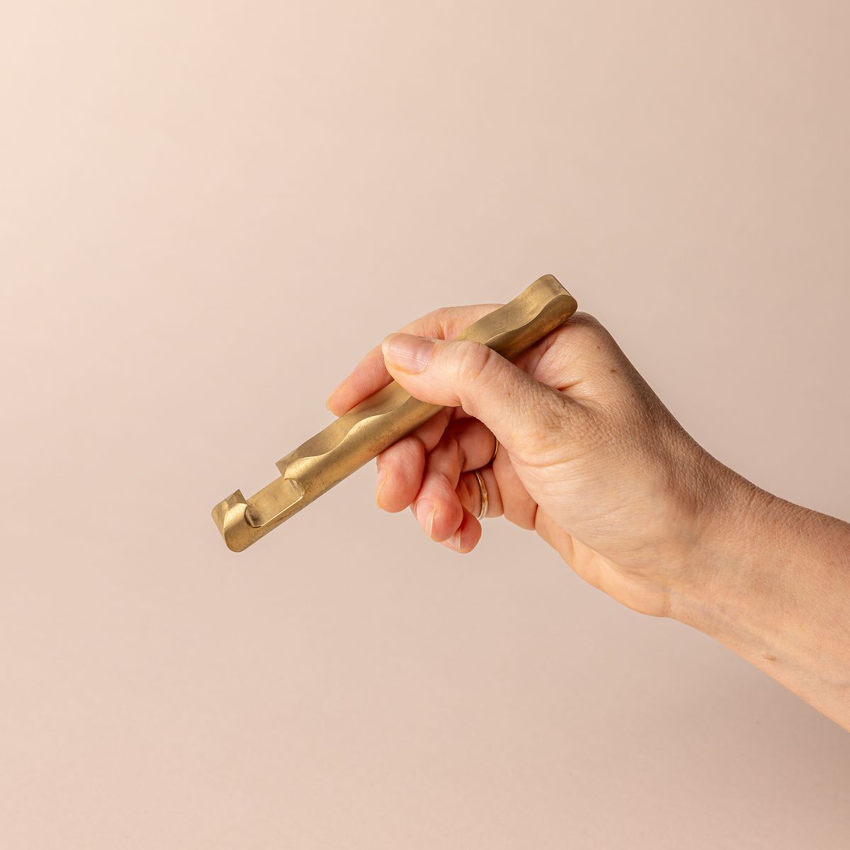 Hand holding a sophisticated brass bottle opener with a simple design and a wave with grooves all along the opener side.
