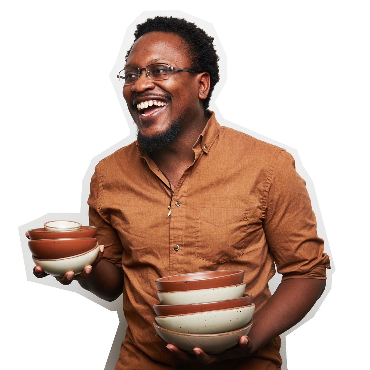 A photo of Jeffery smiling wearing a button down shirt with glasses, and holding stacks of ceramic bowls in white and terracotta colors.