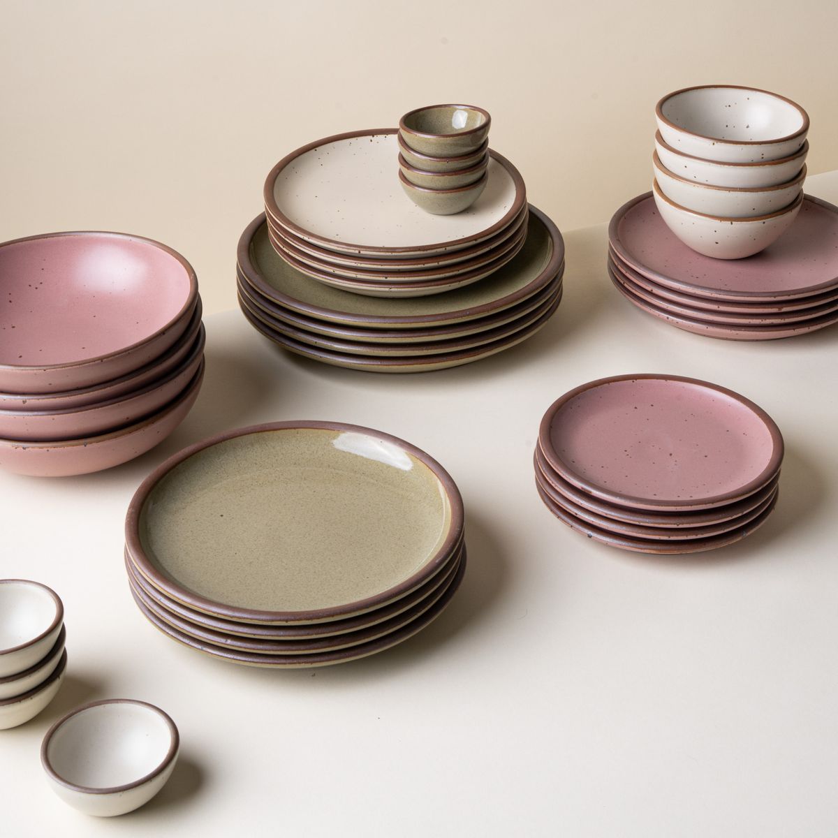 A stack of several plates and bowls in different colors in sets of 4, in grey-green, dusty pink, and off-white colors.