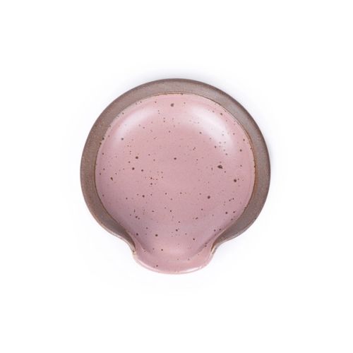 A circular ceramic spoon rest in a dusty mauve pink color featuring iron speckles and unglazed ridge rim