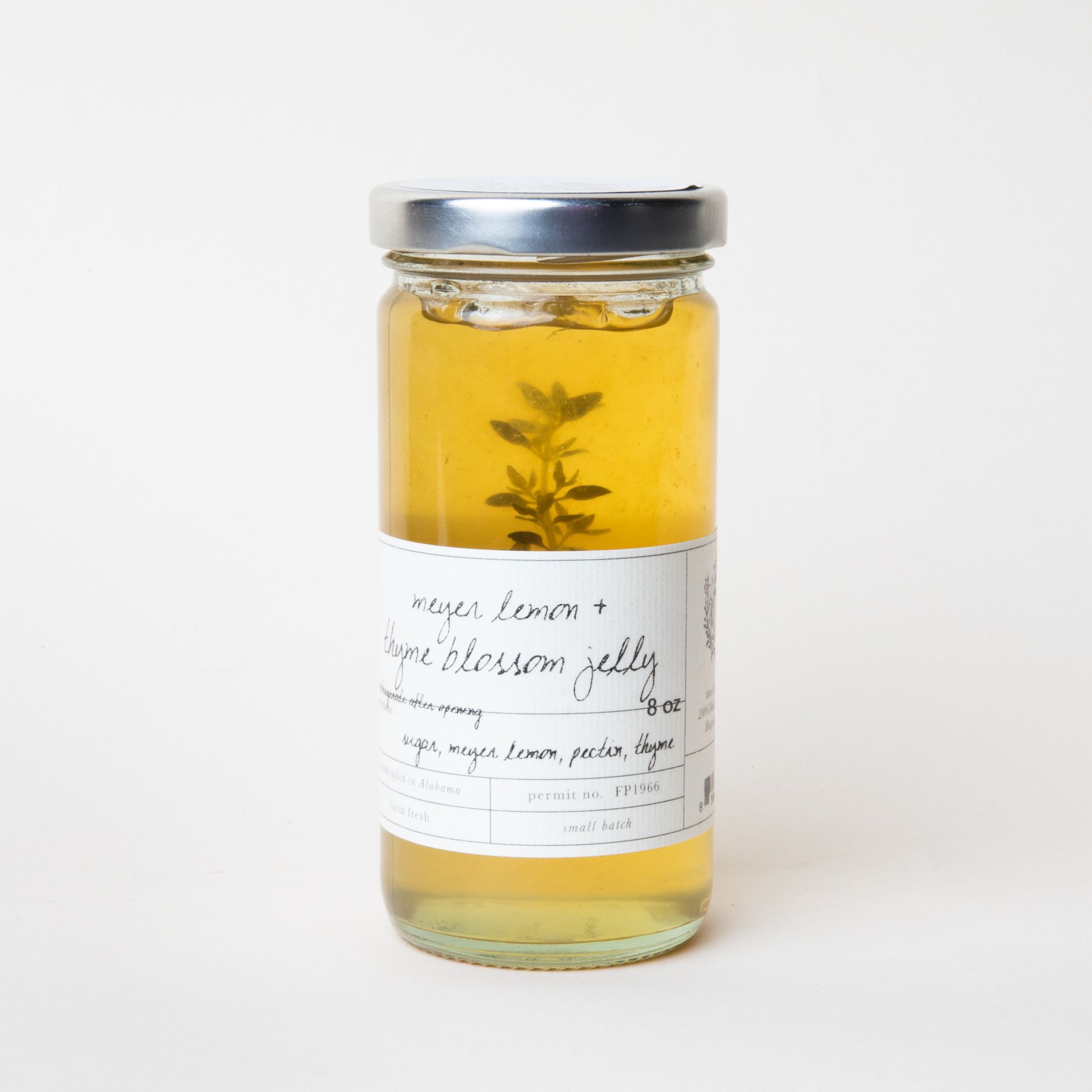 Tall glass jar filled with yellow jelly with a white label that reads "Meyer Lemon and Thyme Blossom Jelly"