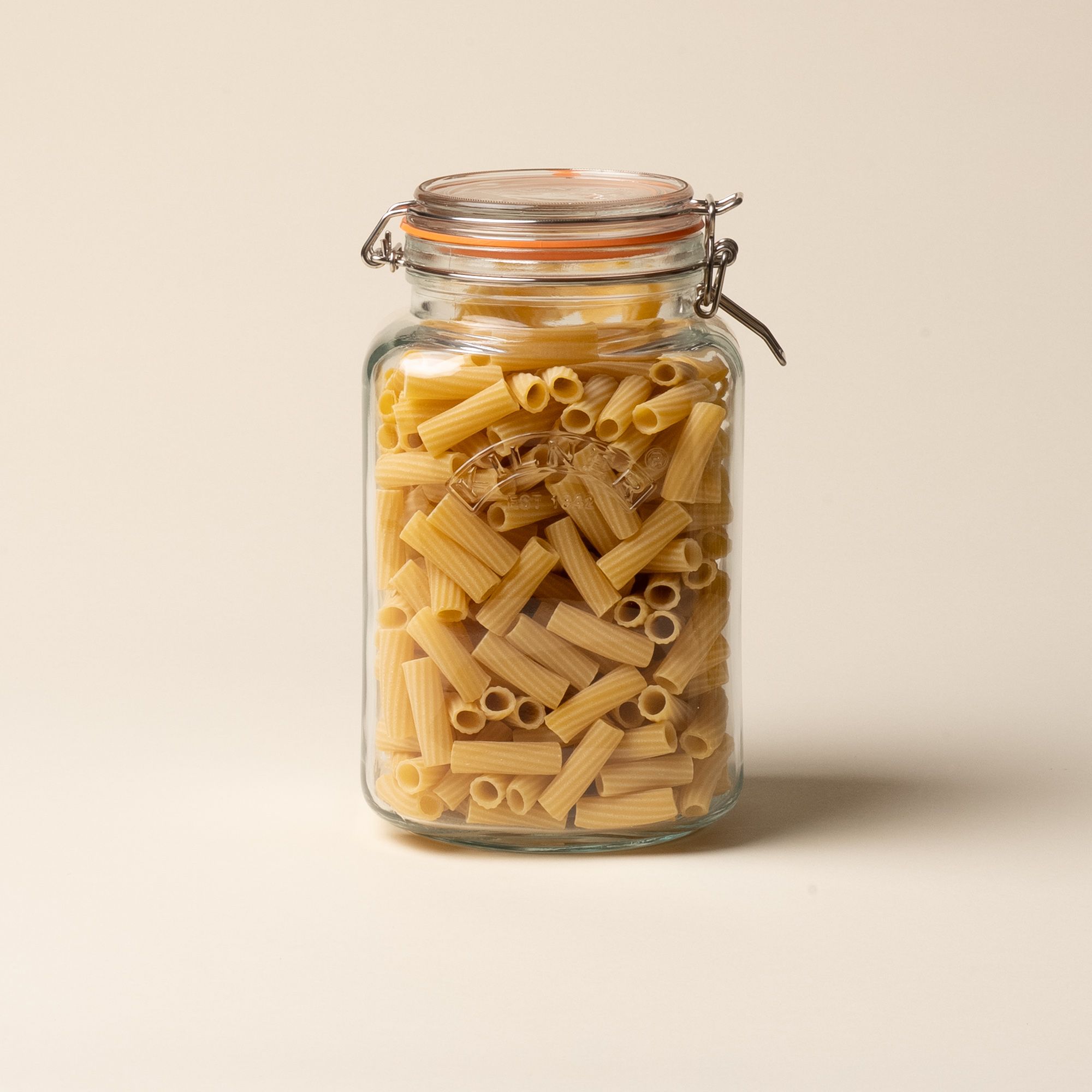 A large storage glass square jar filled with dried pasta and topped with a lid with a rubber seal and steel clip closure.