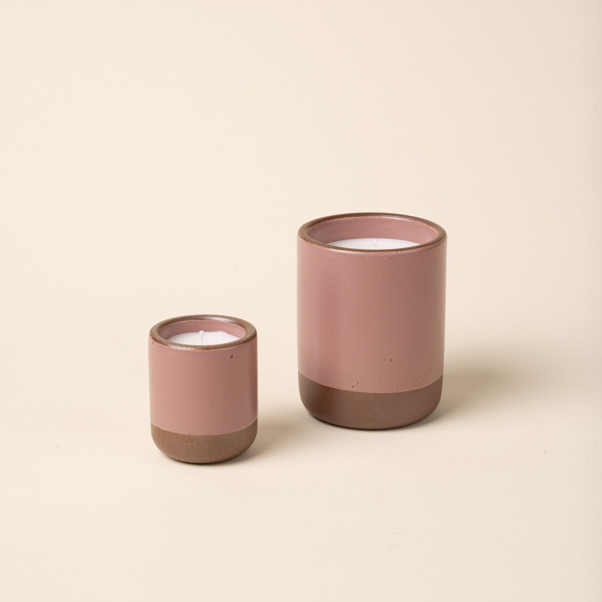 Small and large ceramic vessels in a soft mauve pink color with poured candles inside each.