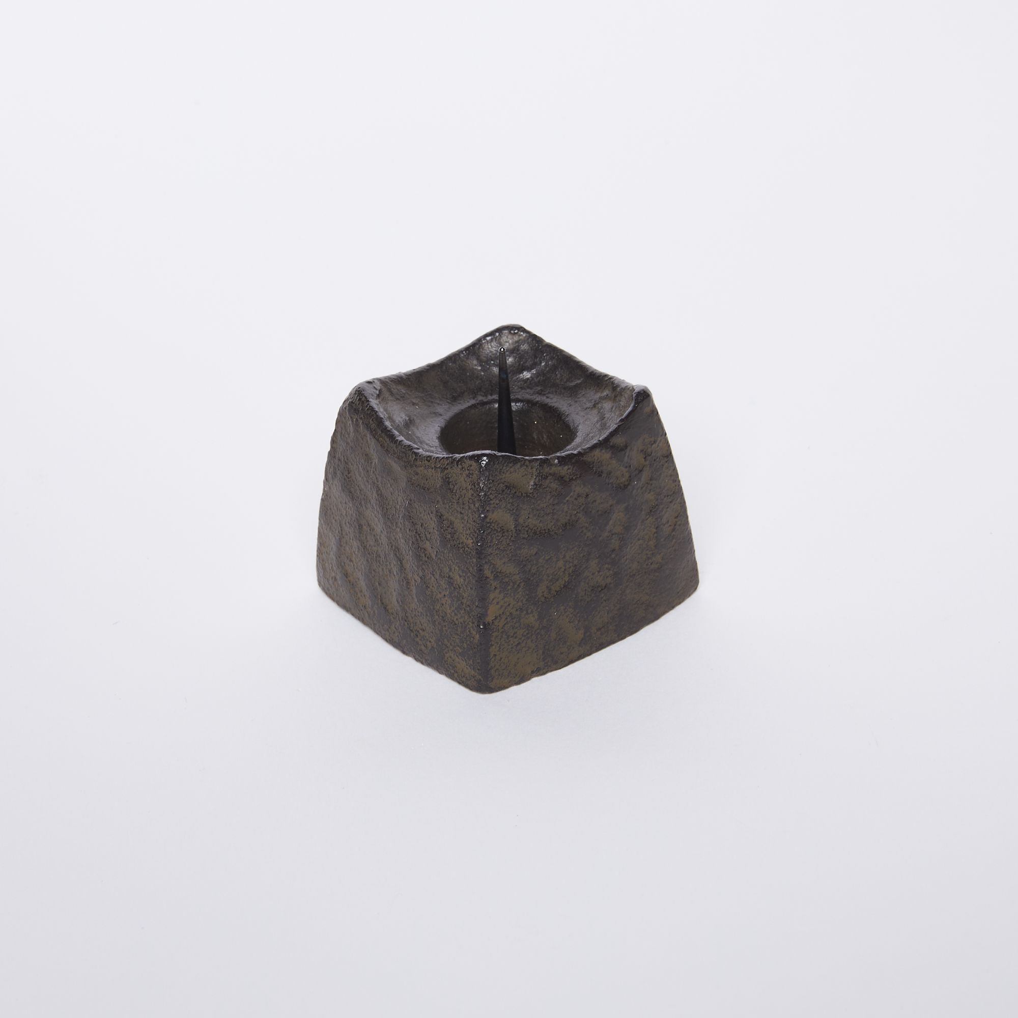 A small black square candle holder with a hammered metal outside and spike in the center