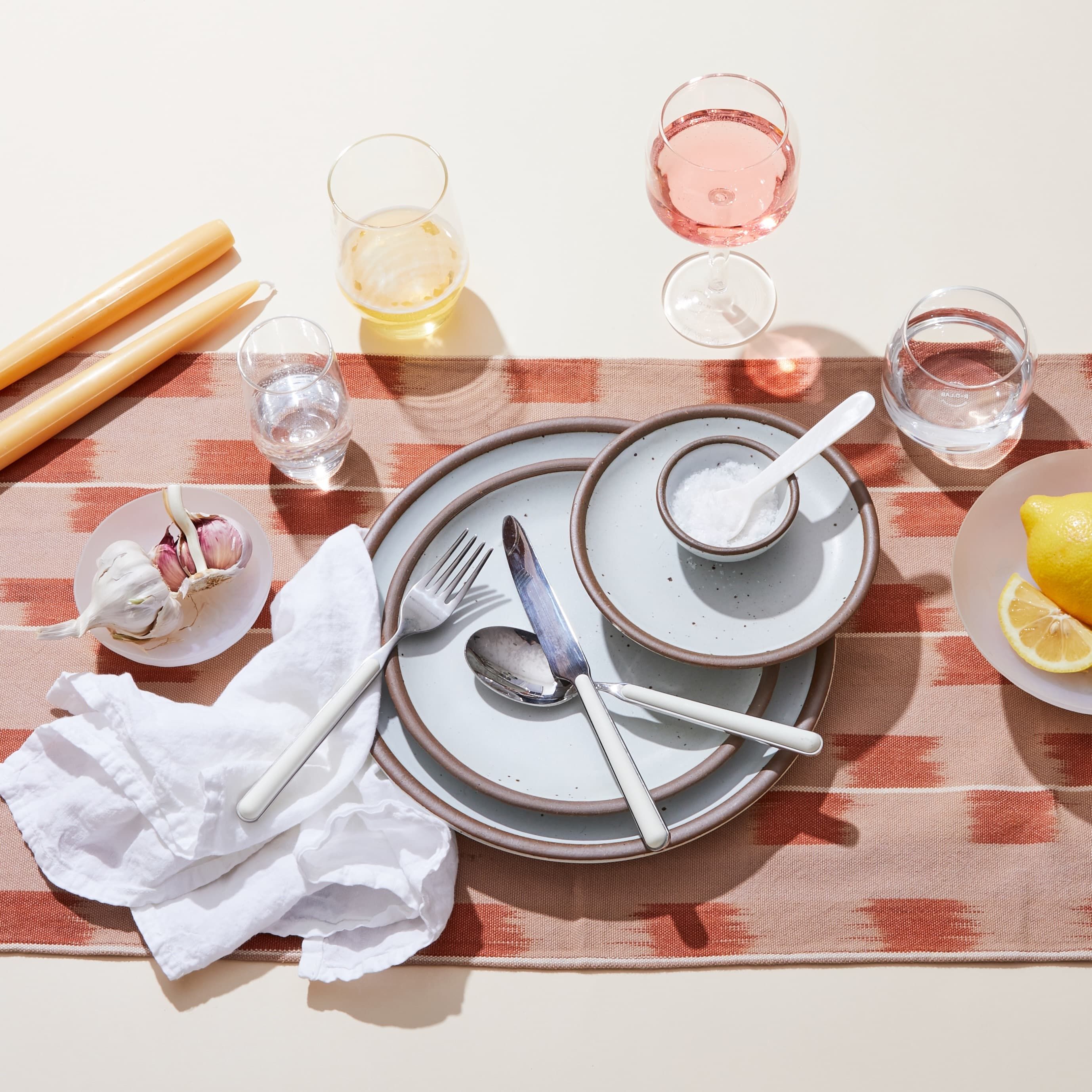 A table setting featuring ceramic white dinner plates, assorted wine glasses, white-handled silverware, and more.