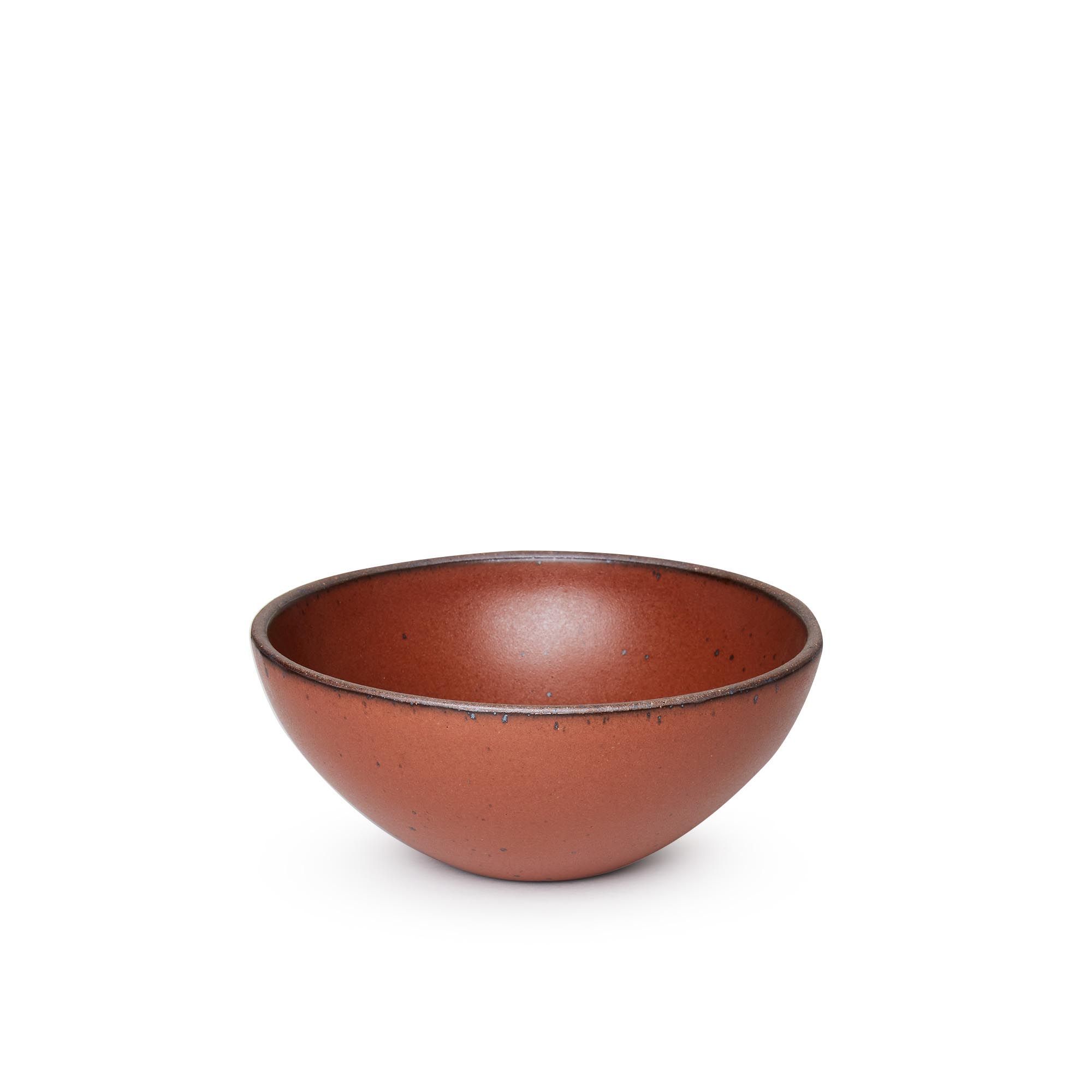 A medium rounded ceramic bowl in a cool burnt terracotta color featuring iron speckles and an unglazed rim