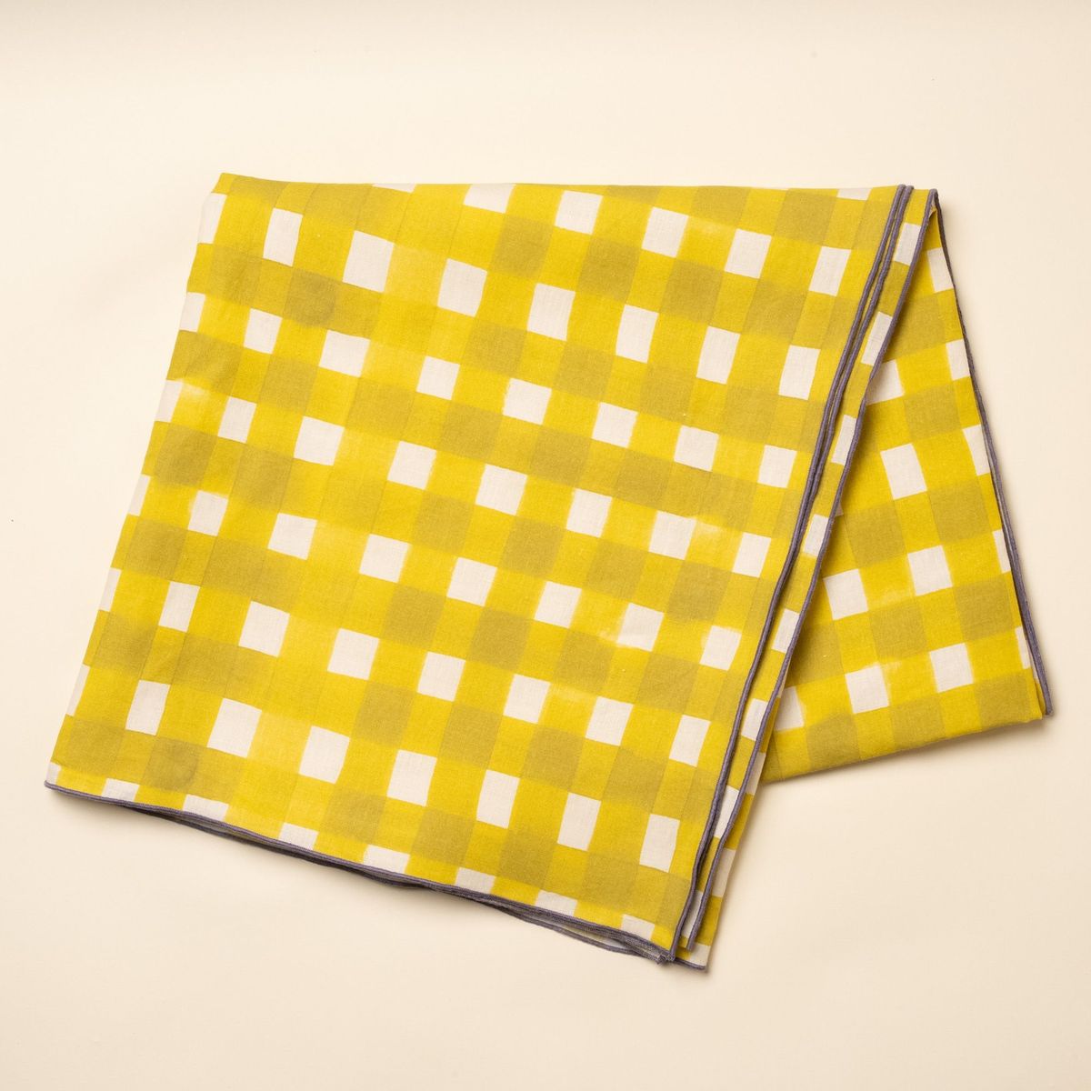 A folded tablecloth featuring a bright yellow crosshatch pattern with purple edges.