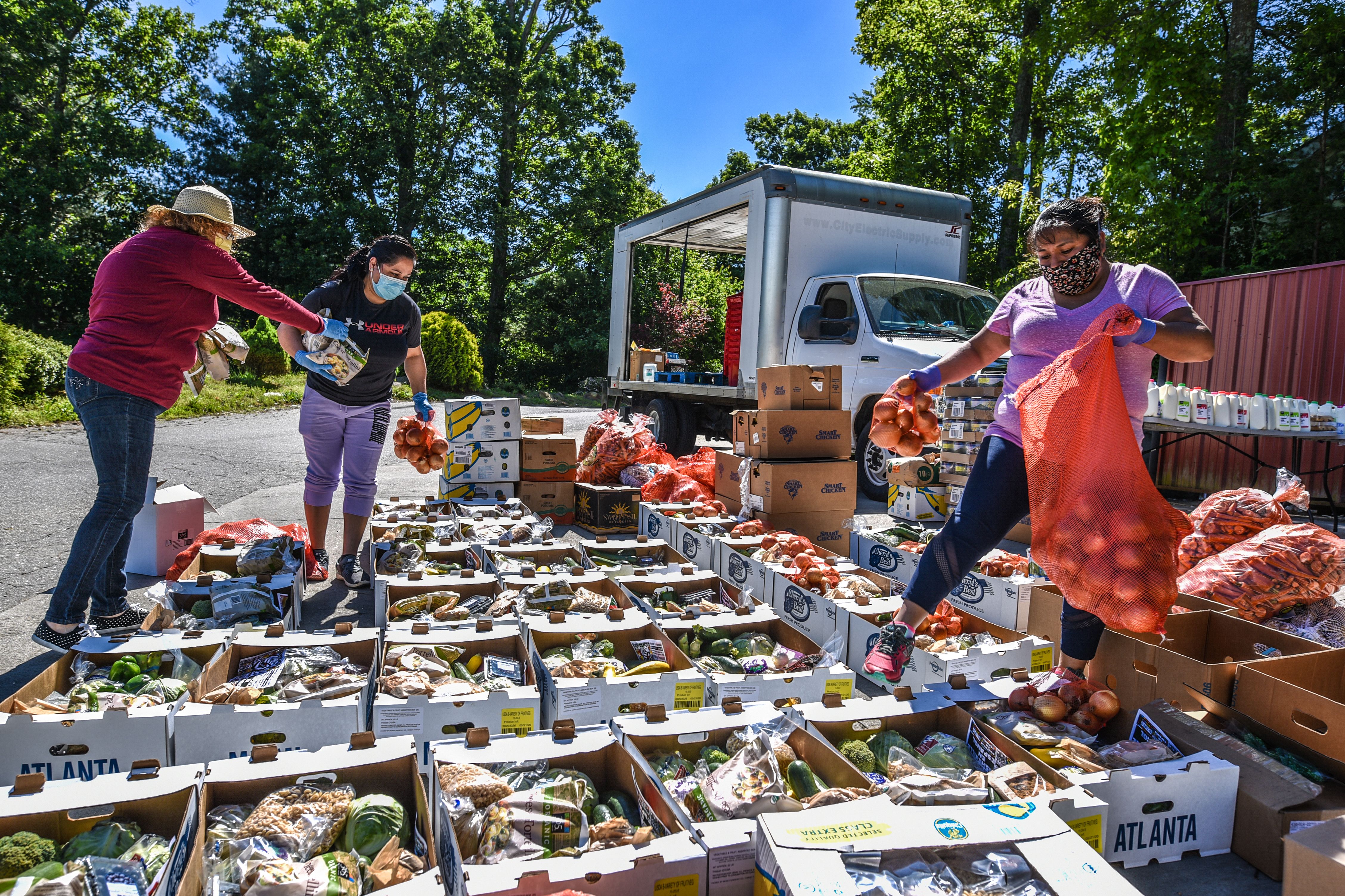 Outside, 3 people are organizing and working on multiple boxes filled with fresh foods