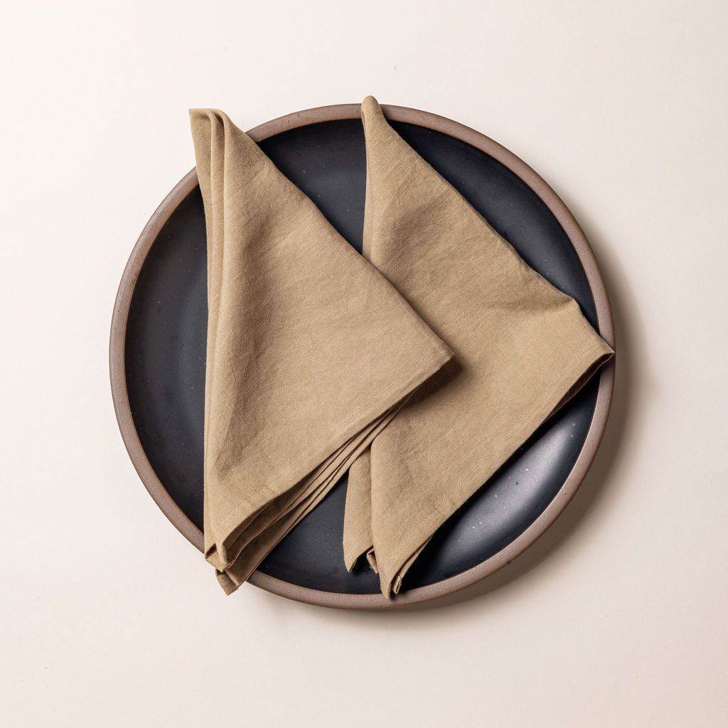 Two warm brown linen napkins folded into triangles on a charcoal ceramic plate.