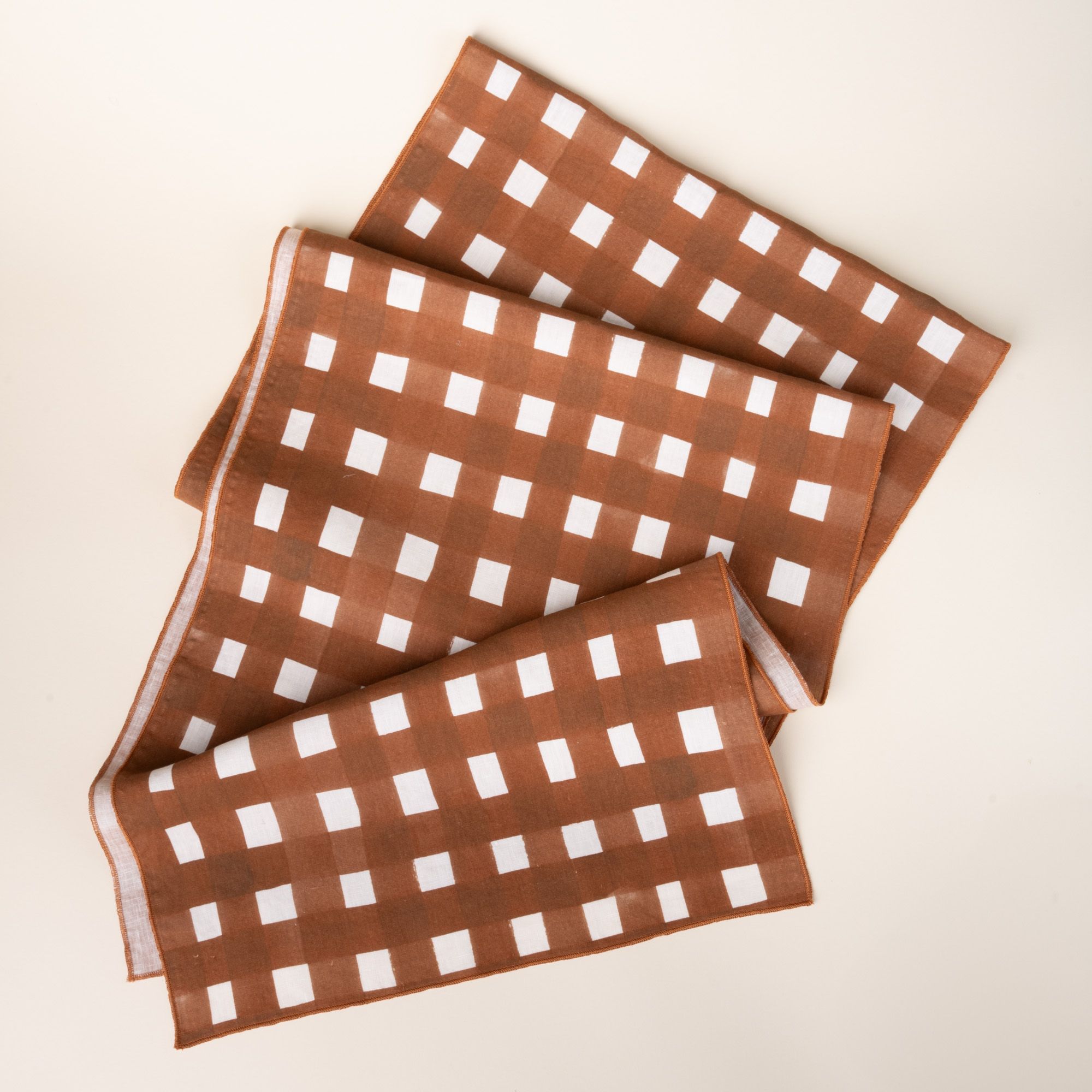 Brown and white crosshatch linen table runner folded neatly on a neutral background.