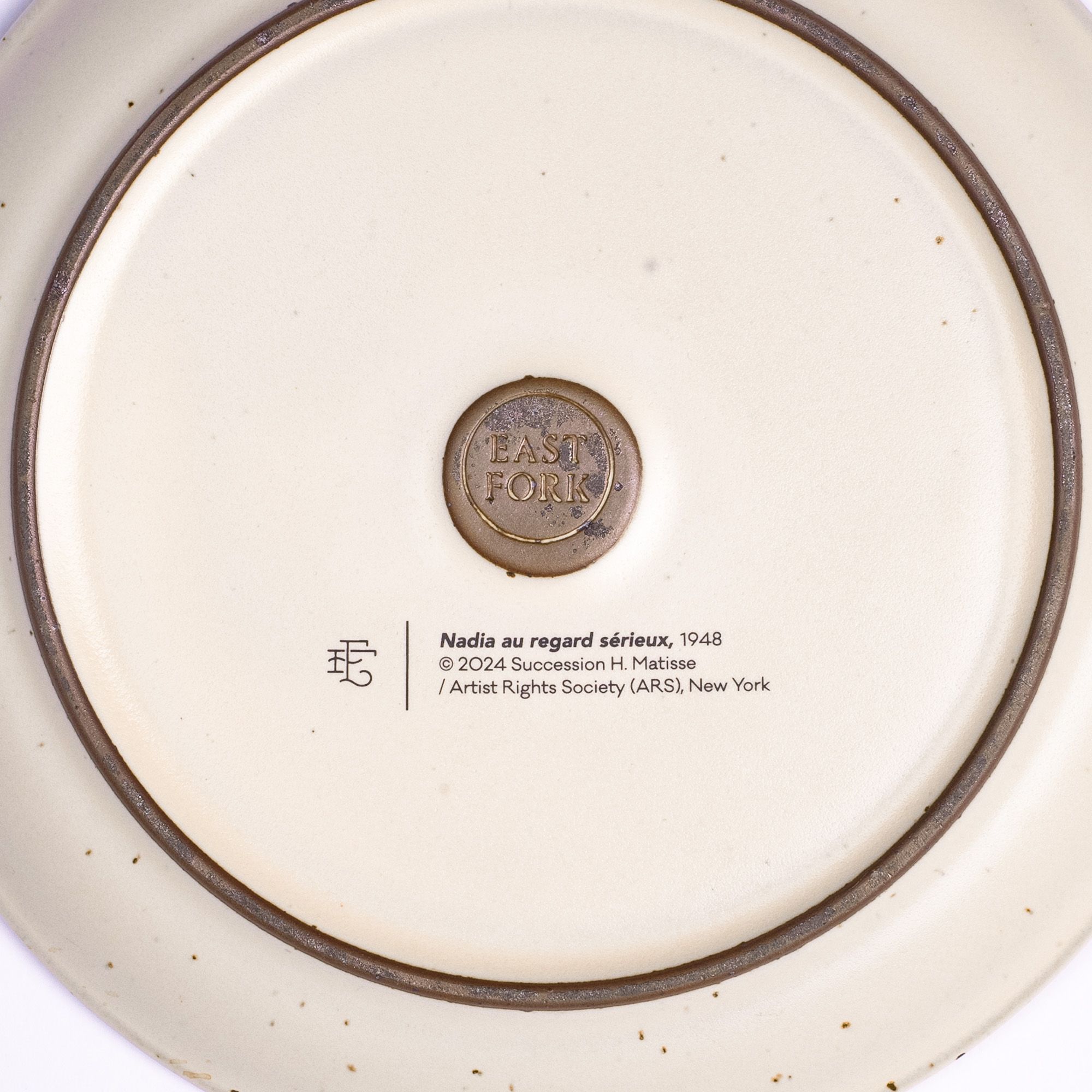 The back of a side plate with an East Fork stamp with a small decal of information about the artwork, Nadia au regard sérieux, by Henri Matisse.