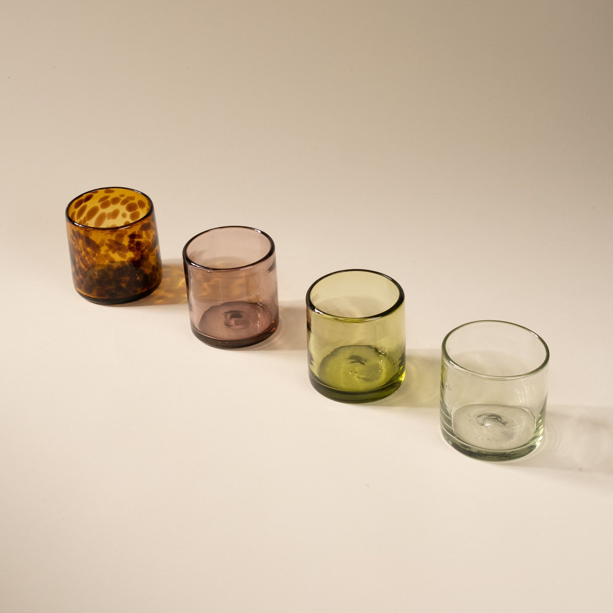 A row of short transparent tumblers glasses in different colors including: tortoiseshell, light plum, olive green, and clear