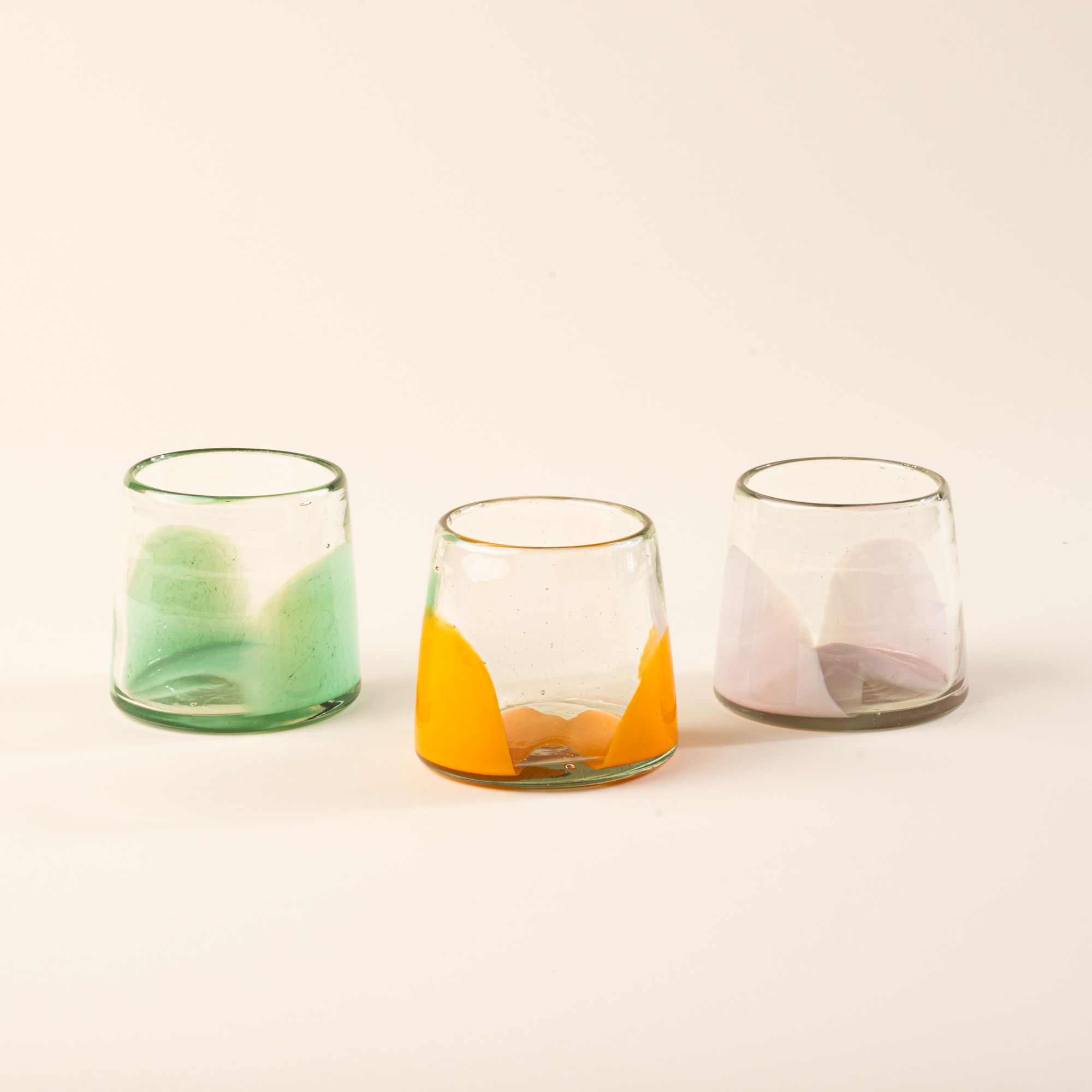 Three short glasses with orange, pastel green, and pale light pink bases