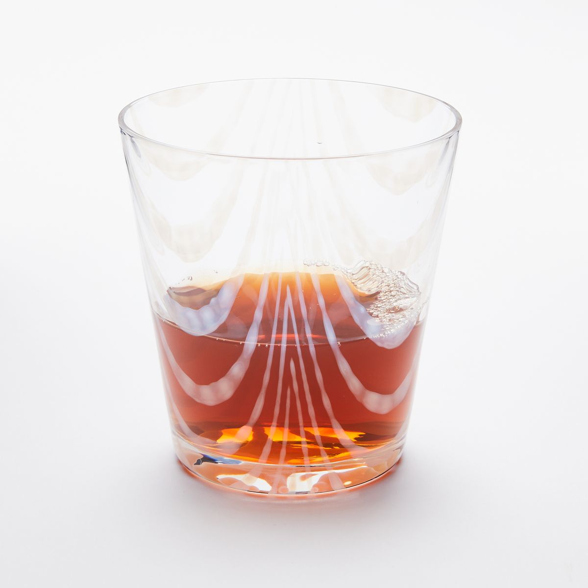 A short clear glass with a delicate ripple pattern, half filled with a drink