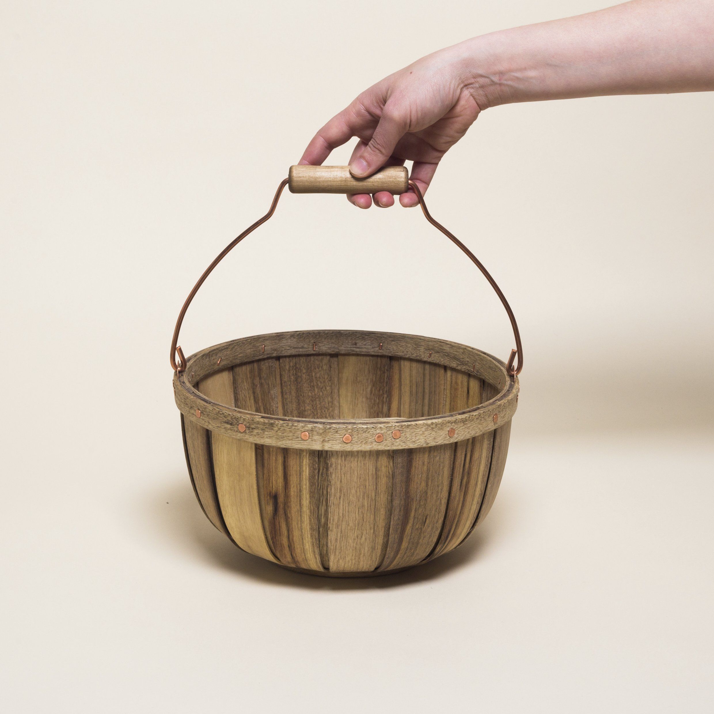 A hand holds the metal handle of a round wooden basket