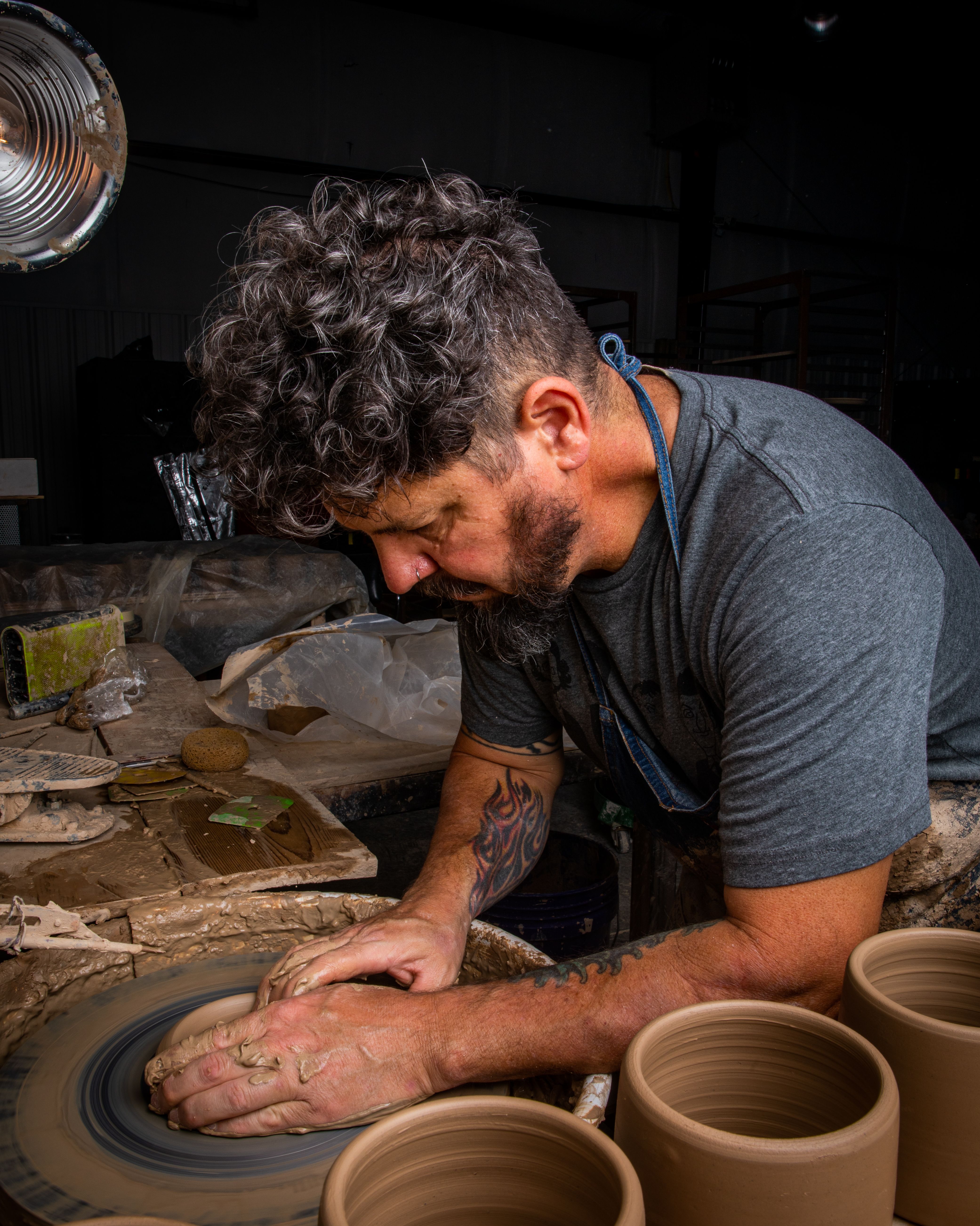 Mike sitting at a potter's wheel forming a utensil holder
