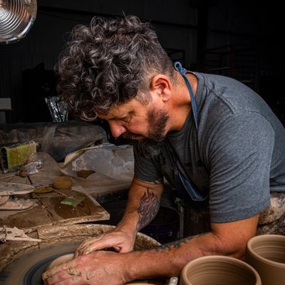 Mike sitting at a potter's wheel forming a utensil holder