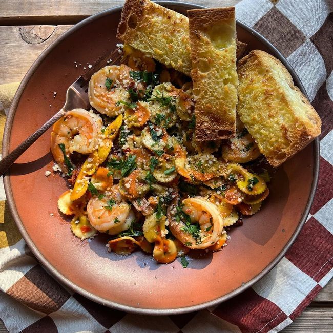 A ceramic coupe plate in a terracotta color filled with a shrimp dish and sliced bread