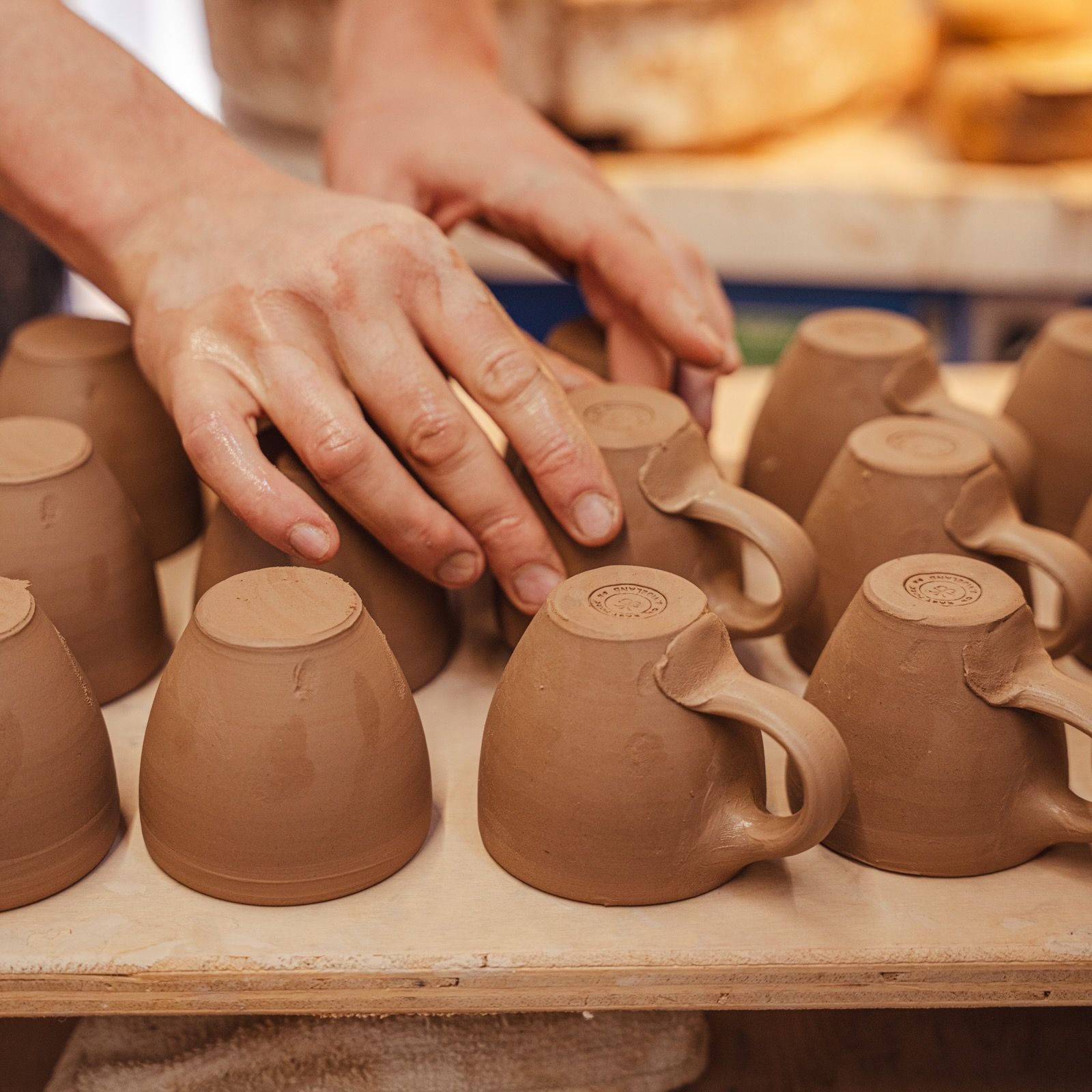 John placing a thrown espresso cup on a piece of wood to dry with rows of other espresso cups