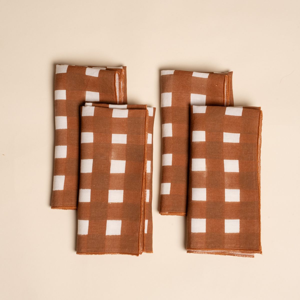 Four folded napkins with a brown and white crosshatch pattern, neatly arranged on a neutral background.