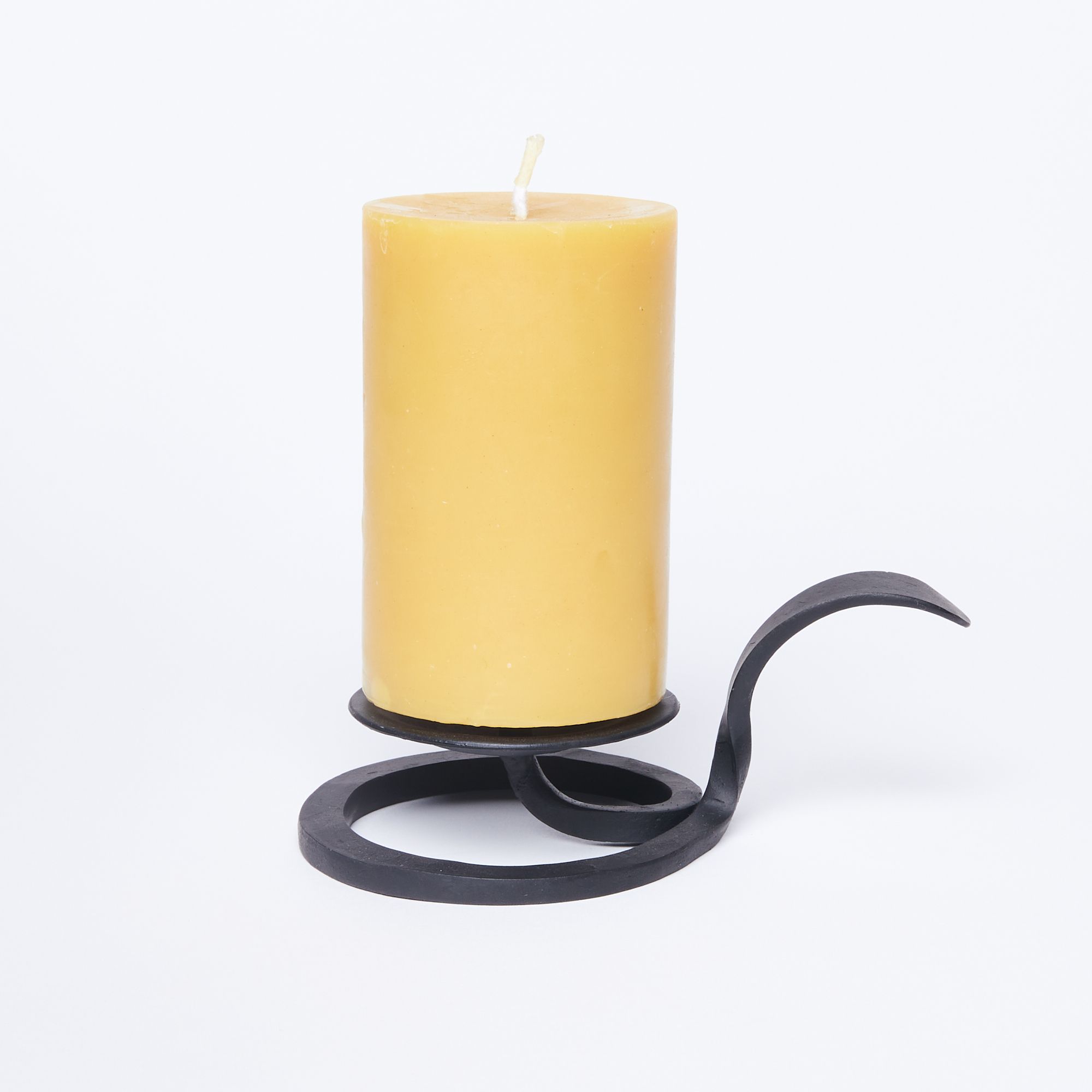 A cylindrical yellow pillar candle atop a cast iron candle stand