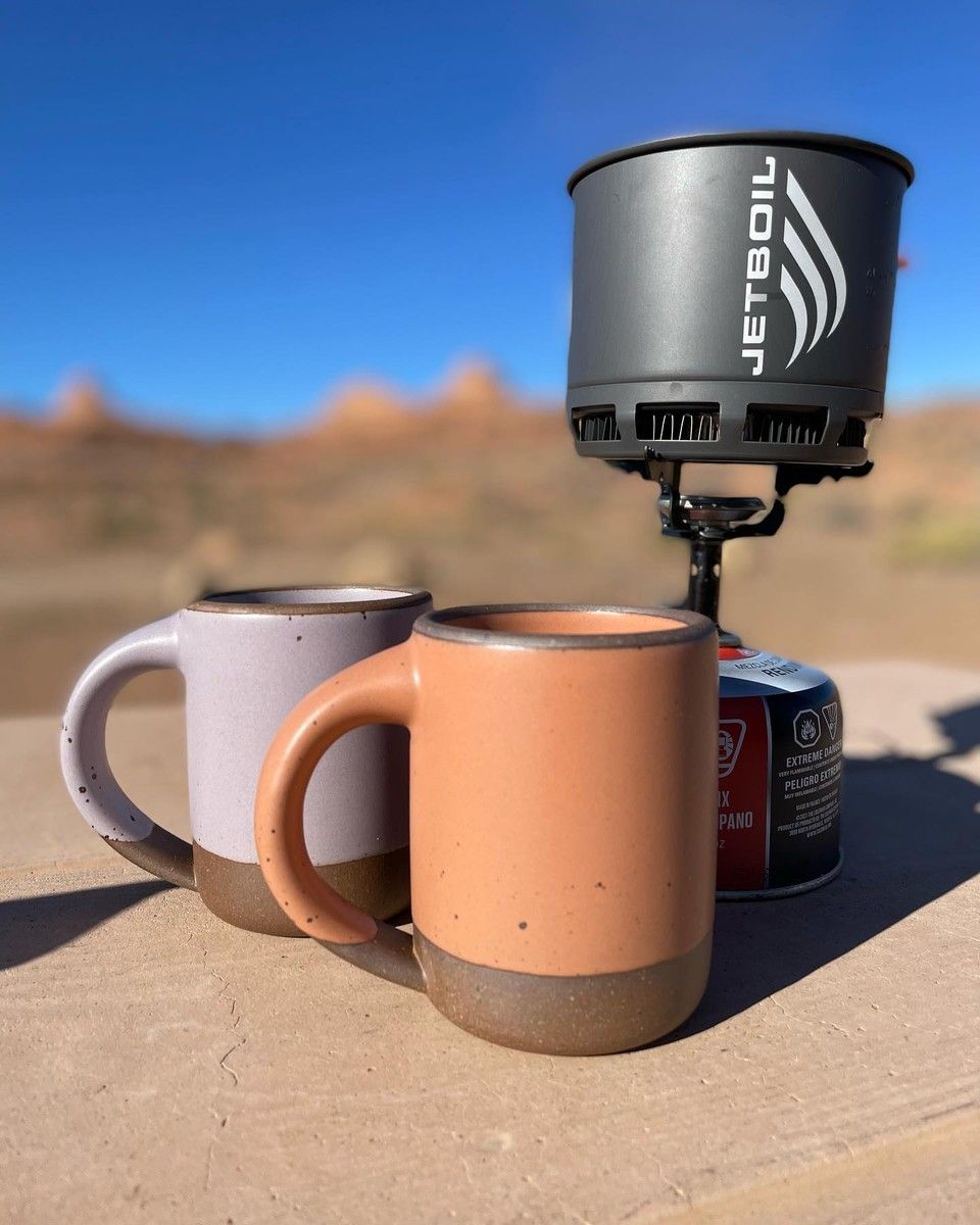 Two East Fork Mugs truly in the wild – sitting on a rock next to a JetBoil camping stove. In the background, the Utah desert.
