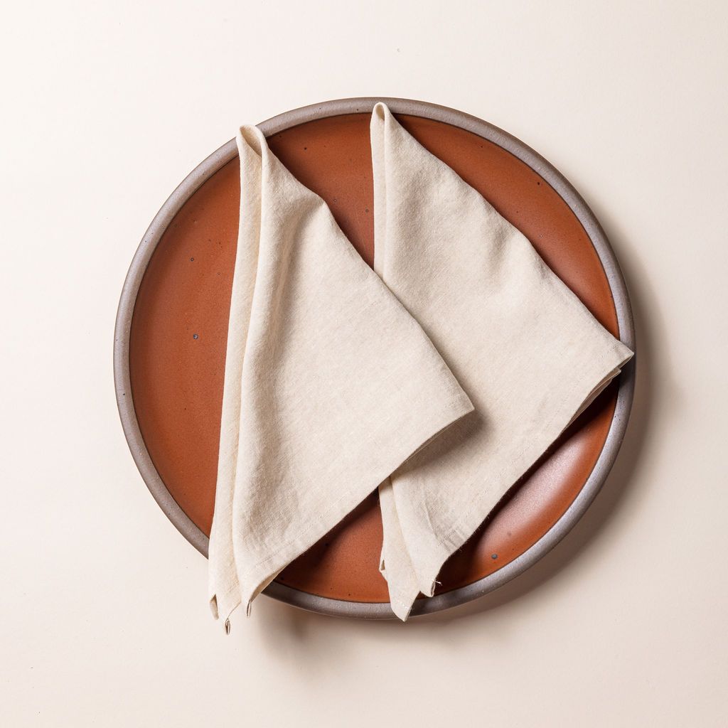 Two off-white linen napkins folded into triangles on a terracotta ceramic plate.