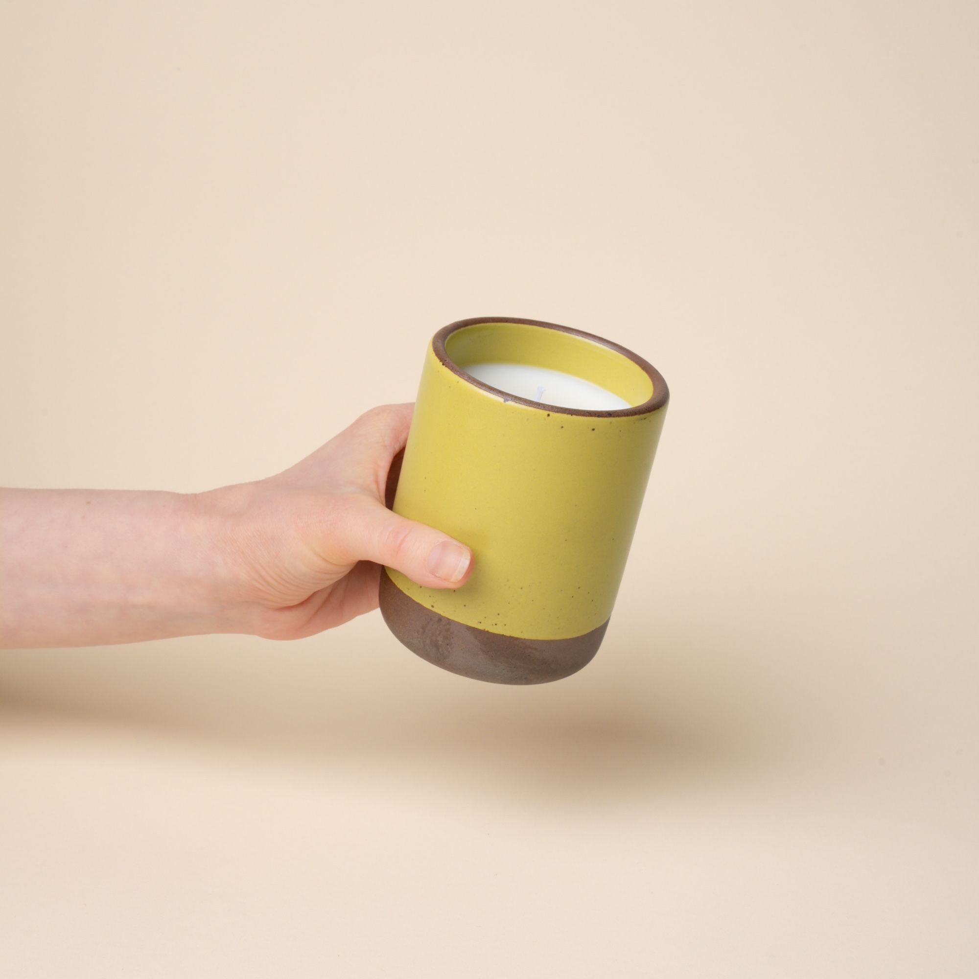 A hand holds a large ceramic vessel in a zesty yellow color with candle inside.