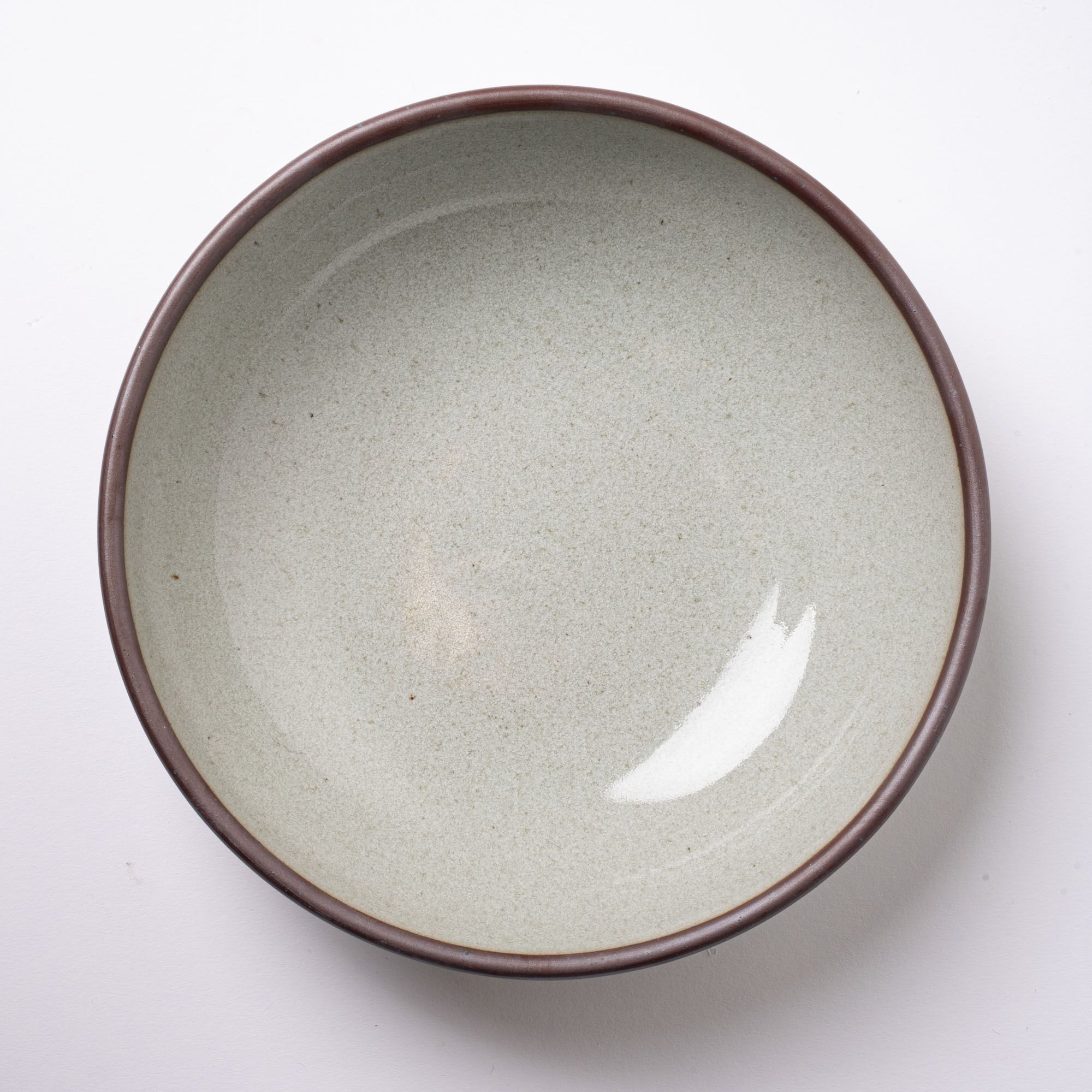 An overhead view of a large rounded ceramic bowl in a reflective icy off-white color with a subtle light pink halo spot.