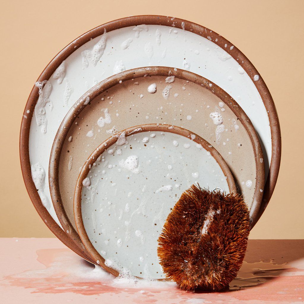 Three plates in various sizes stood on end and flecked with soap and water with a hemp fiber scrubber at lower right corner