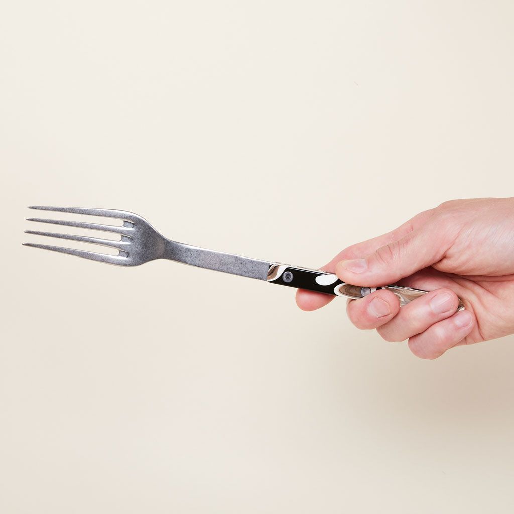 A long-handled serving fork in silver, black and brown, held in a hand