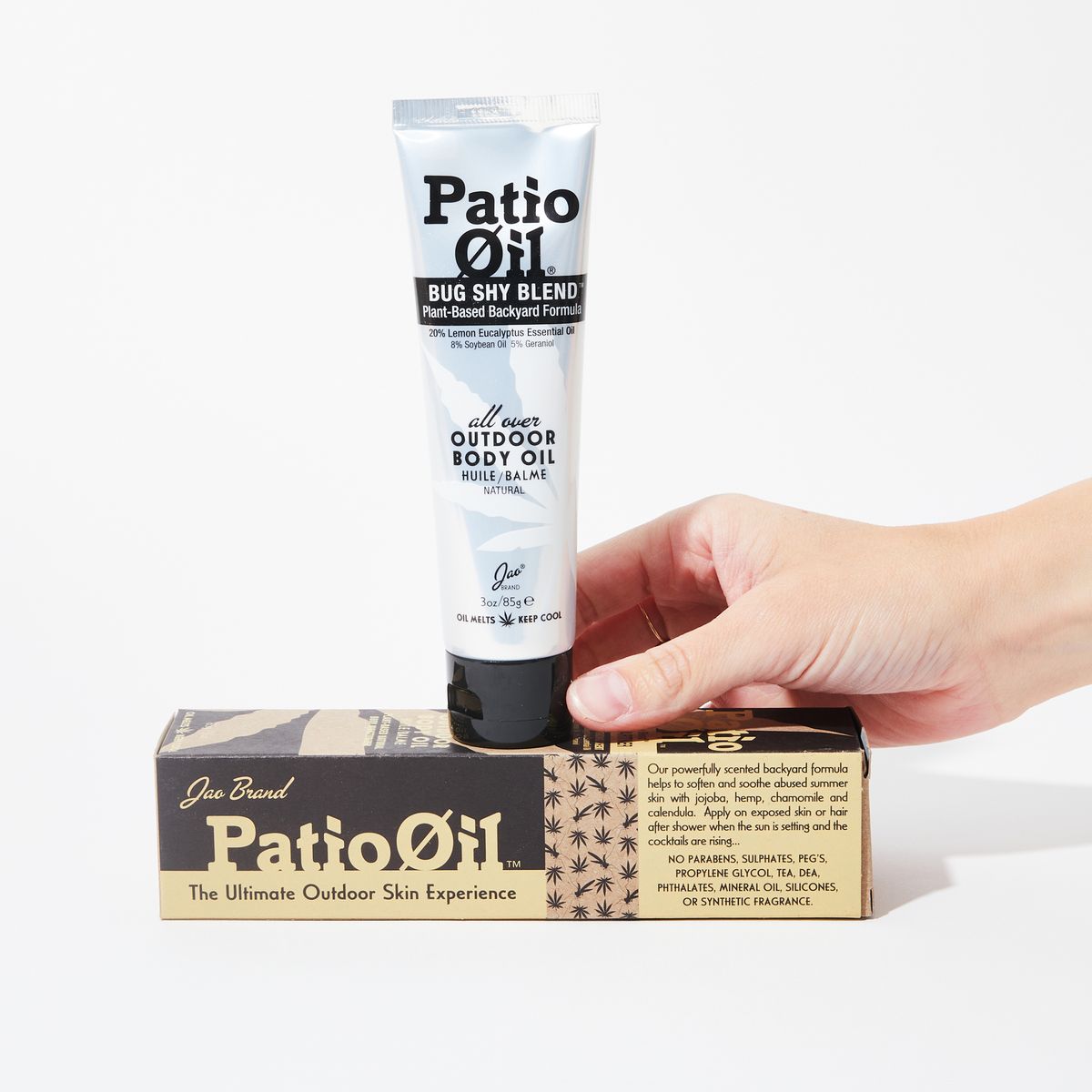 hand holding a silver squeeze tube with black lettering on top of cardboard packaging