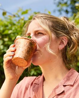 A person outside drinking a cocktail from a copper cup.