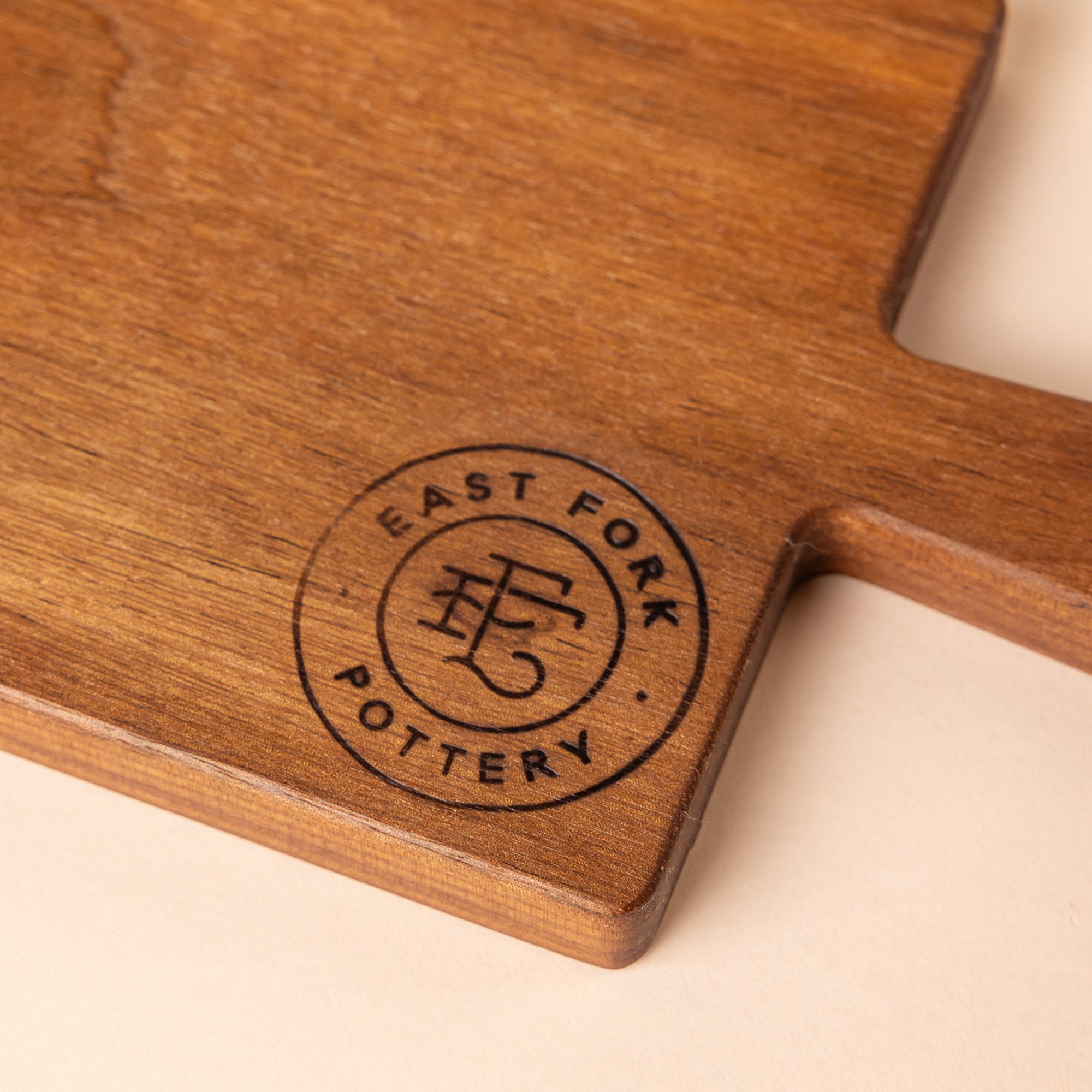 Close up of a stamp on the corner of a wooden bread board. The stamp has a circle with an EF logo and reads "East Fork Pottery".