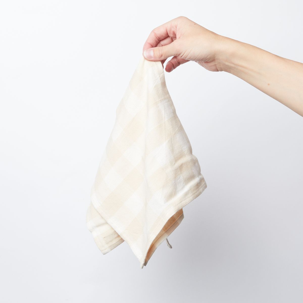 Hand holding a single cream and white gingham cotton napkin from the corner