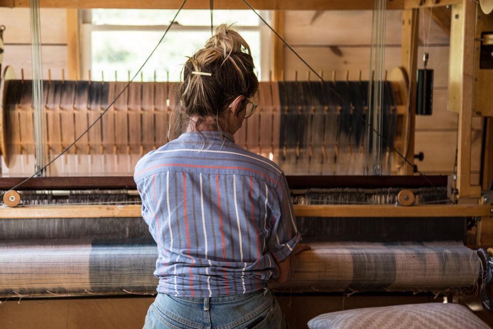 A person sits at a weaving loom with their back to the camera.