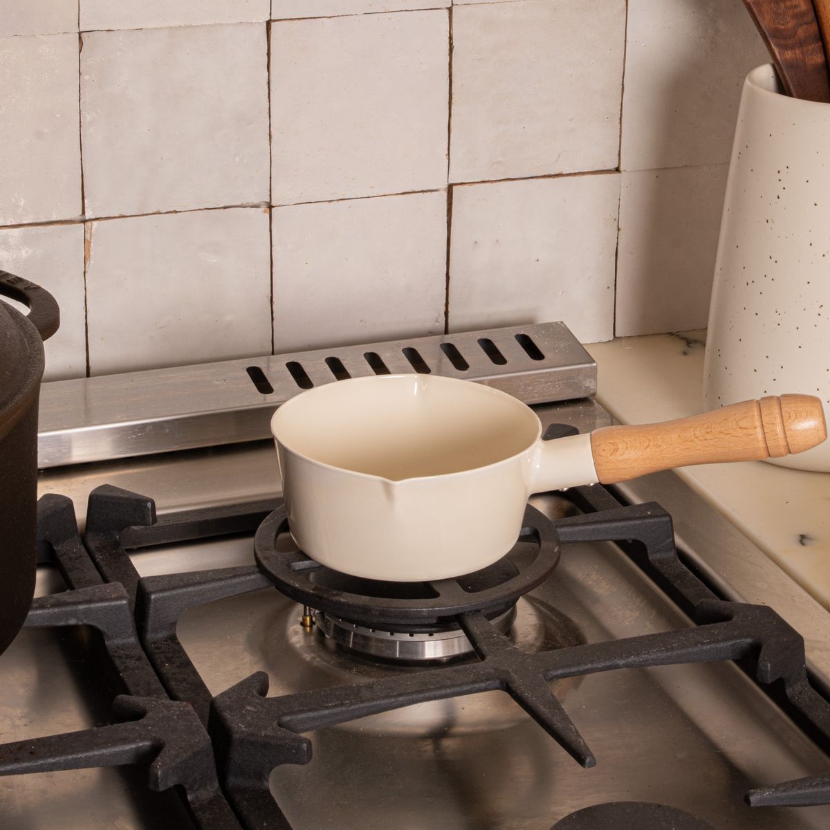 A white enamel pot with simple spouts on the side with a wooden handle, sitting on a gas stove top burner