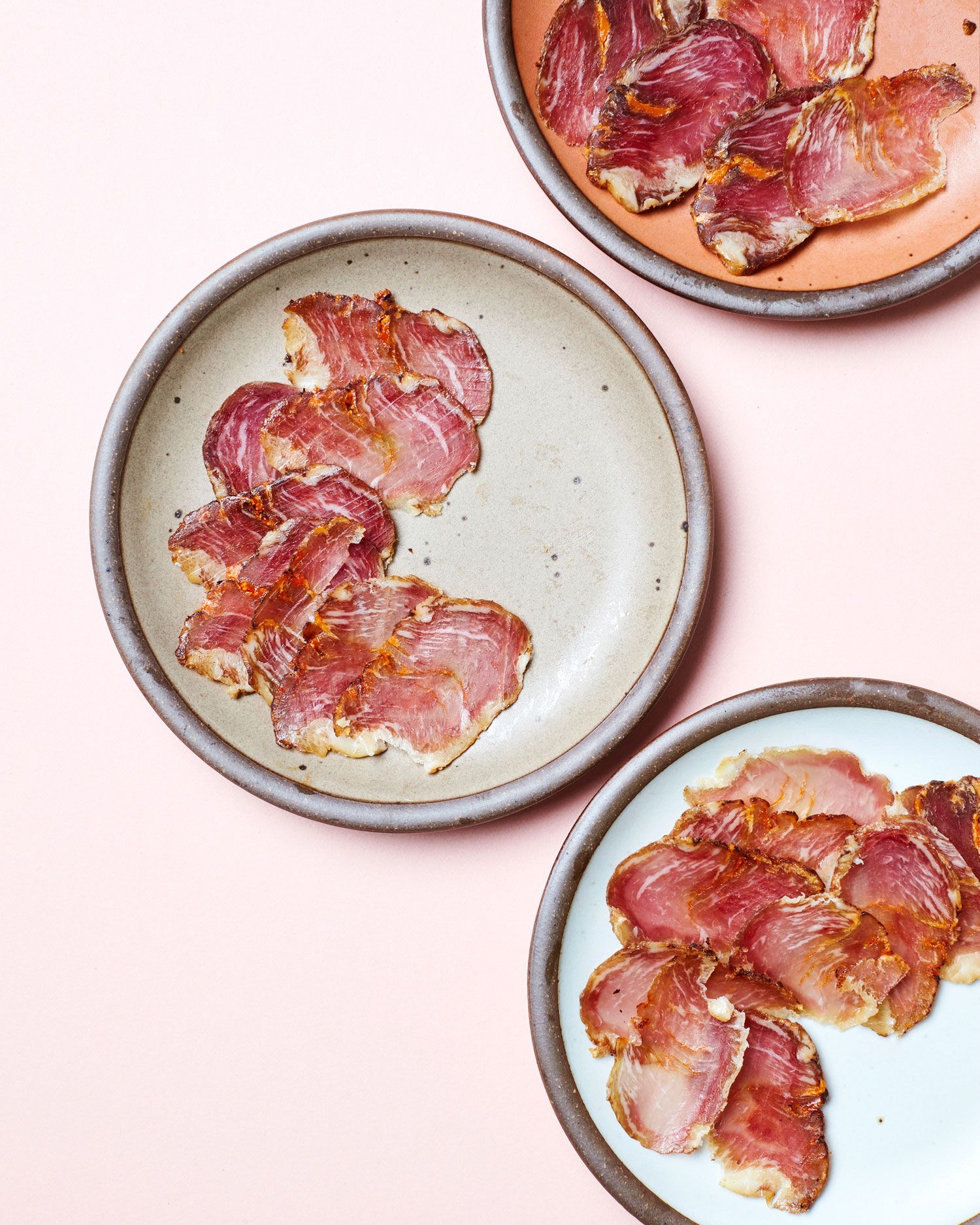 Ceramic plates in a warm pale brown, peach, and white, are plated with thin slices of meat.