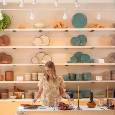 In a retail setting, there is a large wall of dinnerware display ceramic pieces and a worker arranging a table setting in the foreground.