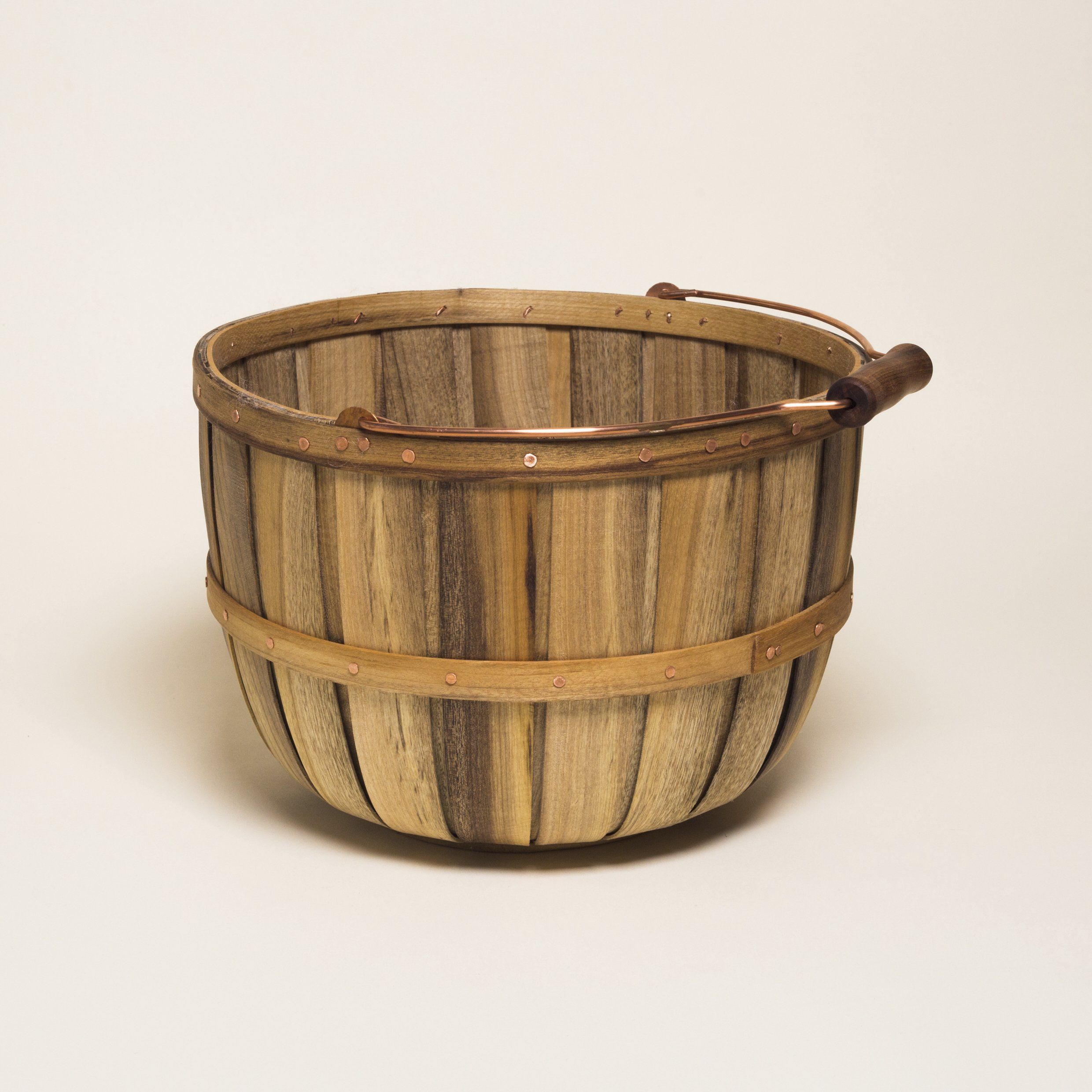 A large tall round rustic wooden basket with a metal and wood handle