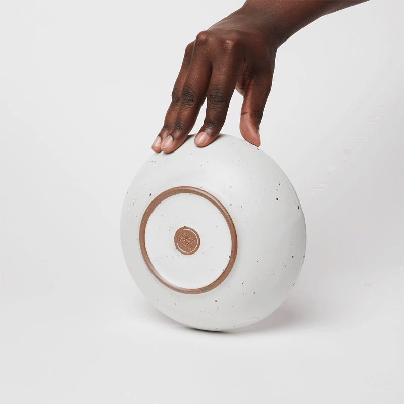 A gif of a hand holding a shallow everyday bowl, spinning it around, and then another hand placing a small shallow bowl and nestling it inside the first bowl.