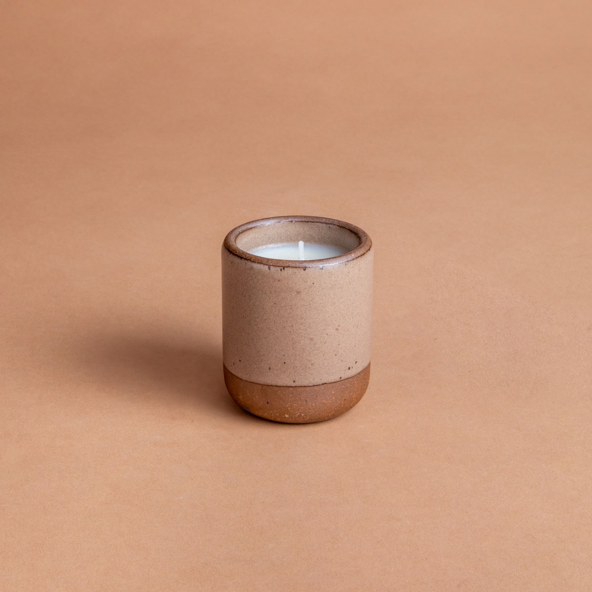 Small ceramic vessel in a warm pale brown color with candle inside.