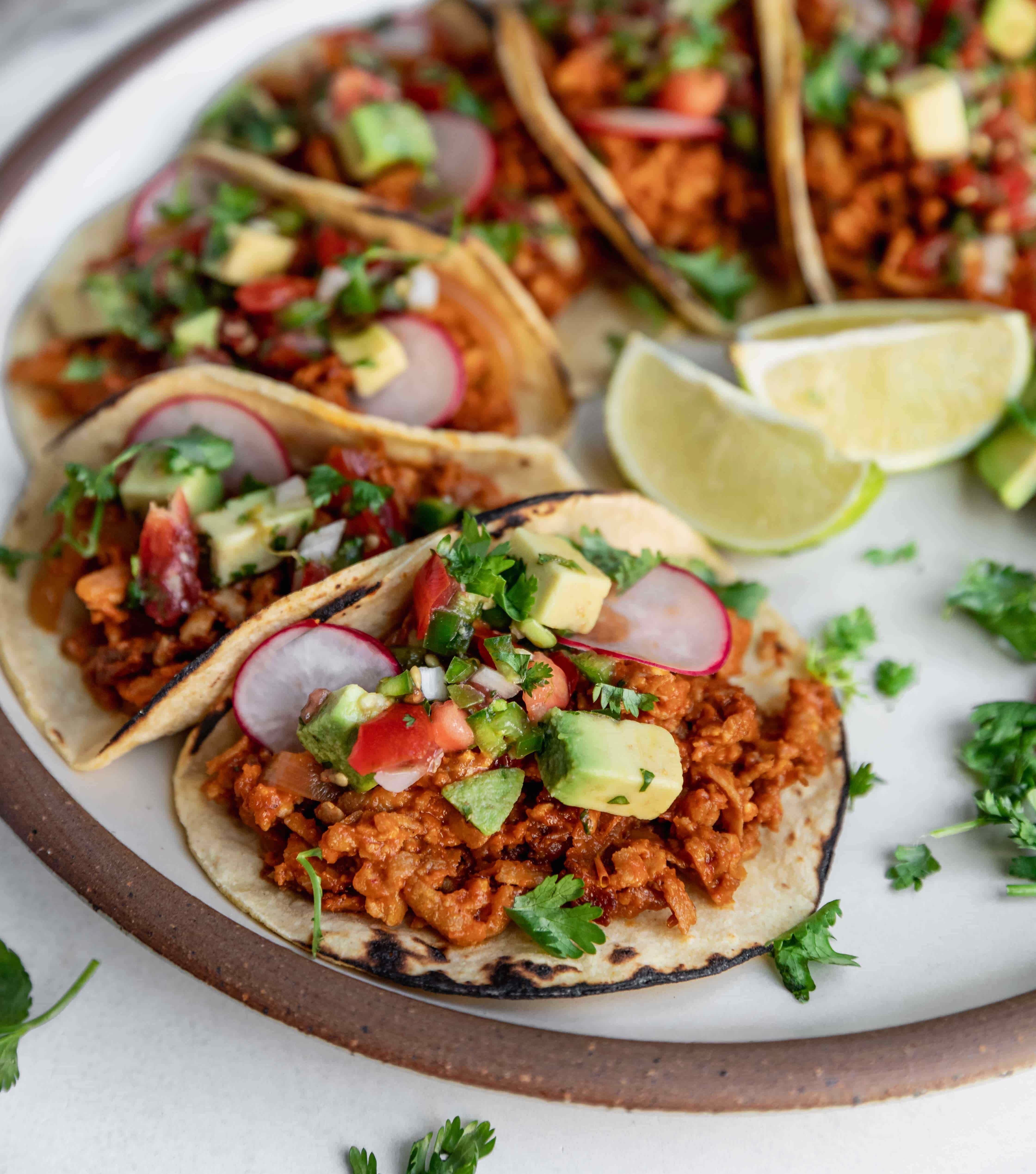Corn tortilla tacos with cilantro and lime wedges on a ceramic white plate.