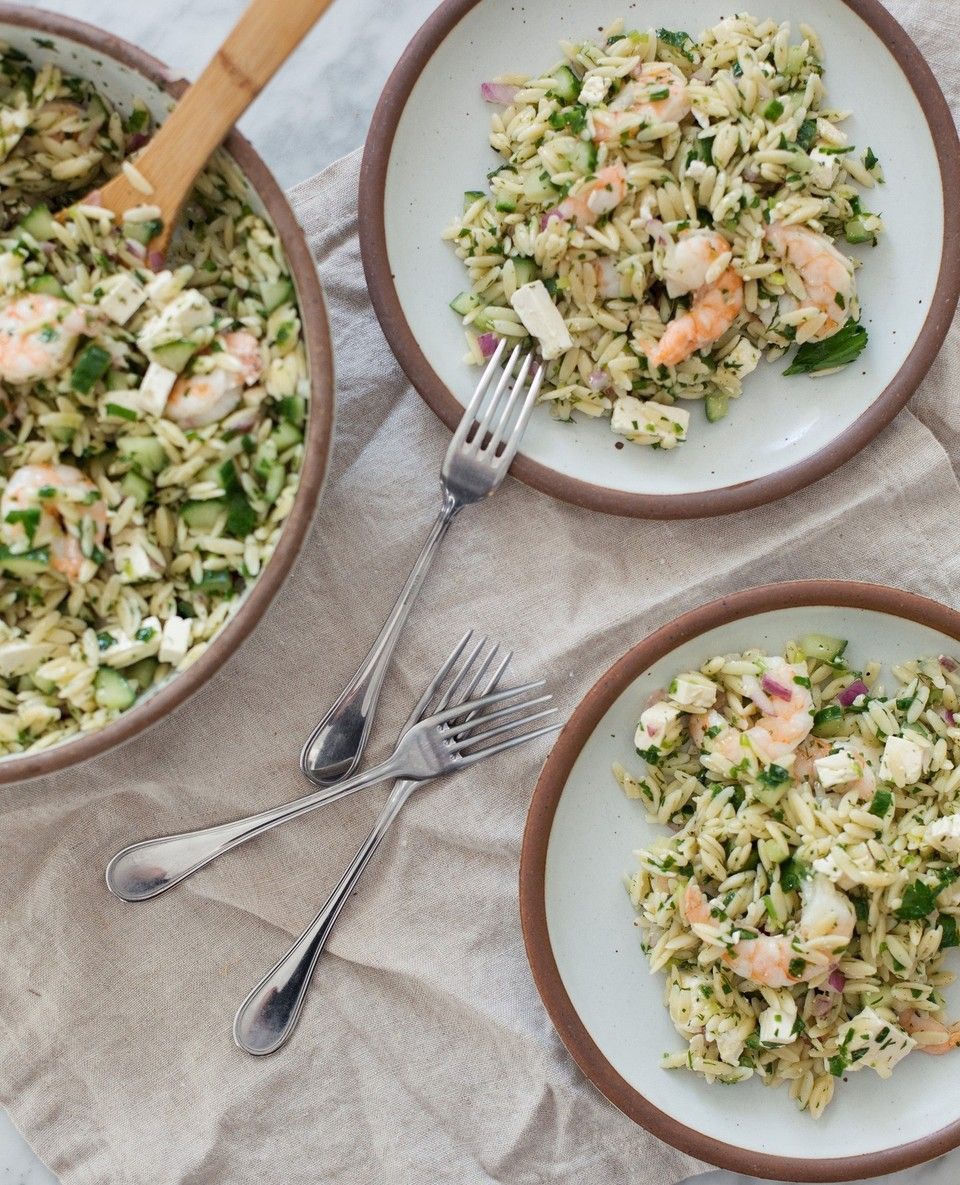 Ceramic plates in a cool white color filled with a shrimp pasta salad and silverware.