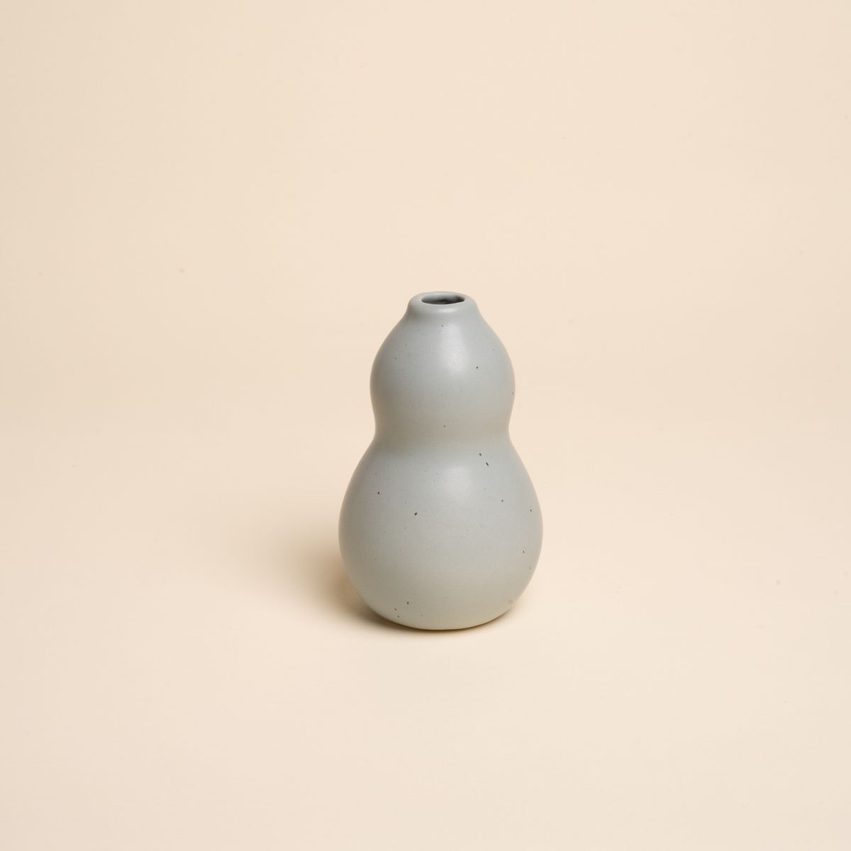 Small blue-grey ceramic vase with a curvy shape and subtle speckles, set against a soft beige background.