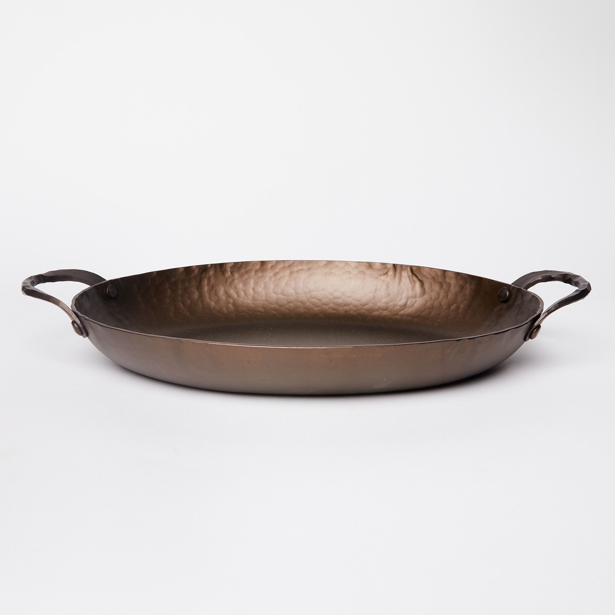 A hammered metal oval roasting pan with handles on both sides